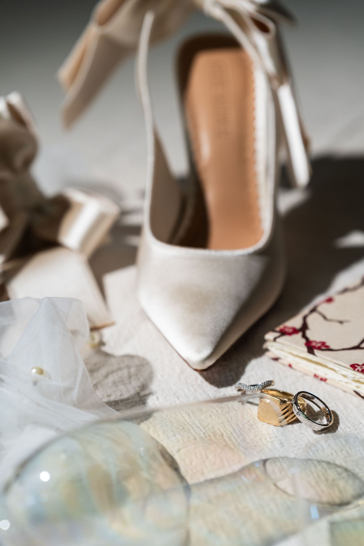 Elegant ivory satin wedding heels with ribbon ties displayed alongside gold rings and bridal accessories.