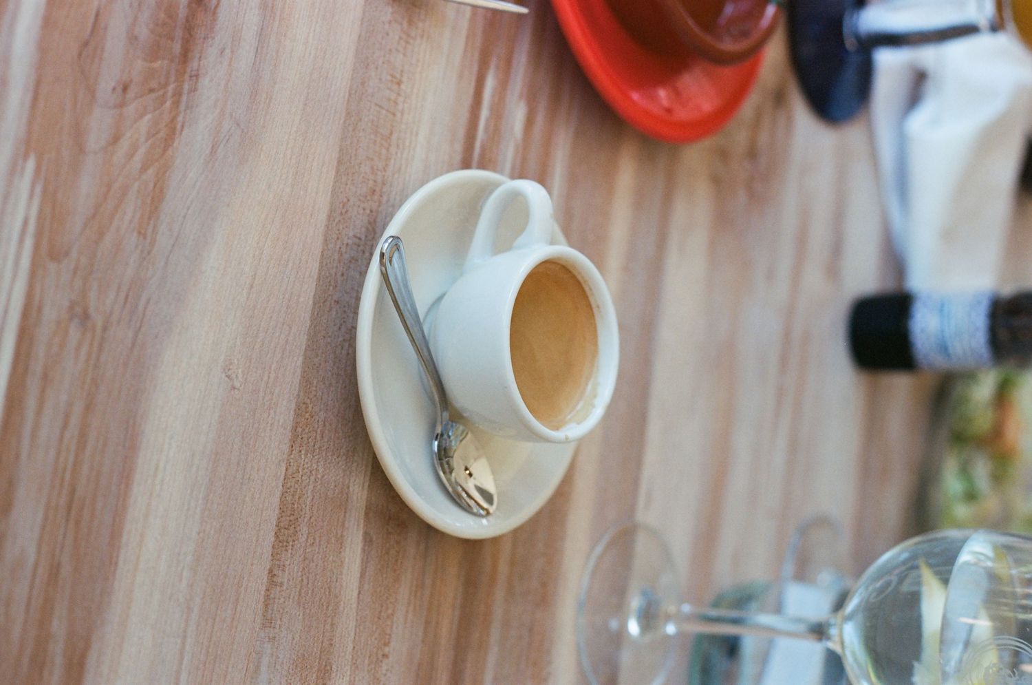 Empty white ceramic coffee cup with spoon on saucer placed on a wooden table in a cafe.