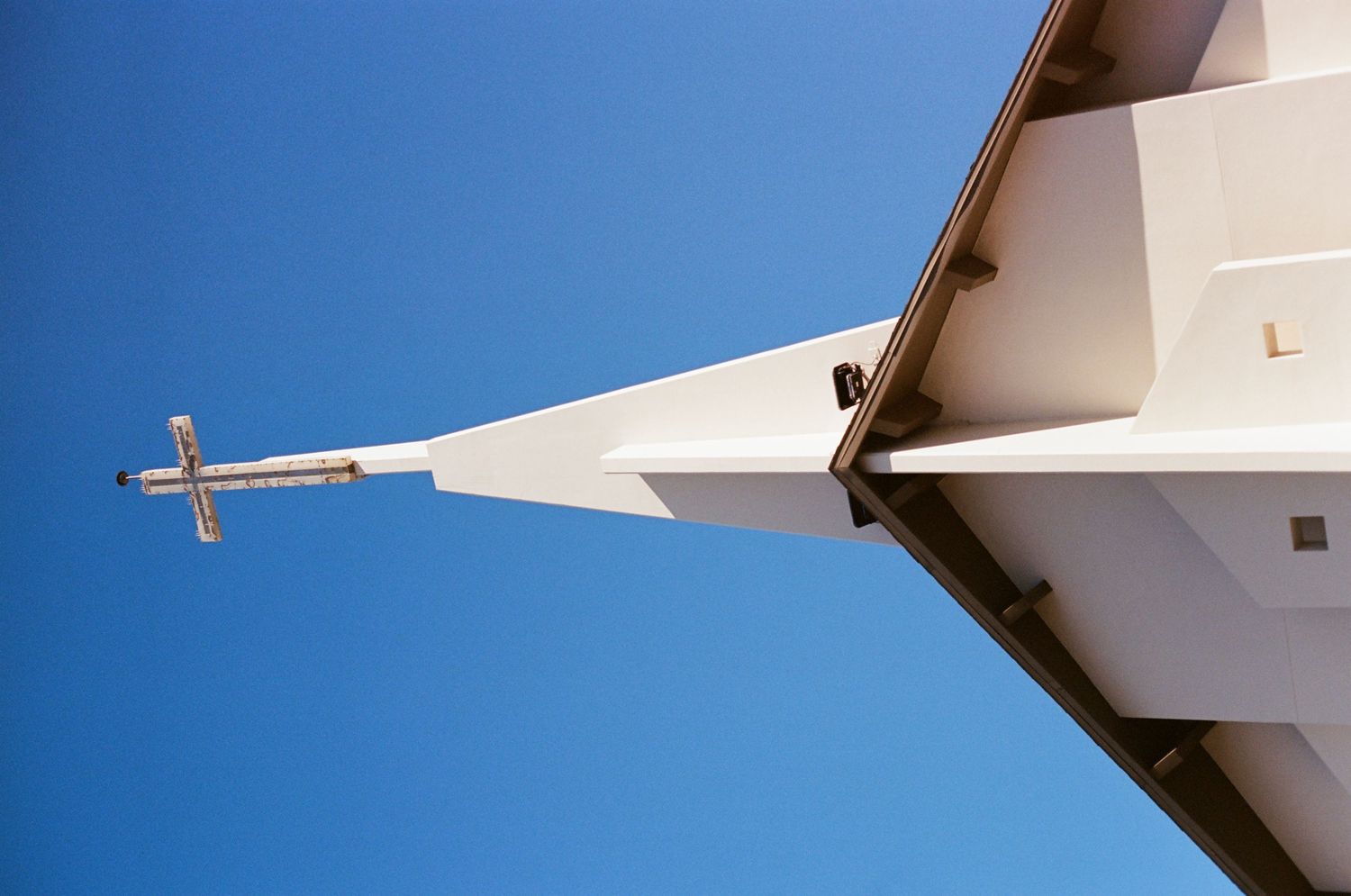 Low angle view of white church steeple with cross against a bright clear blue sky.