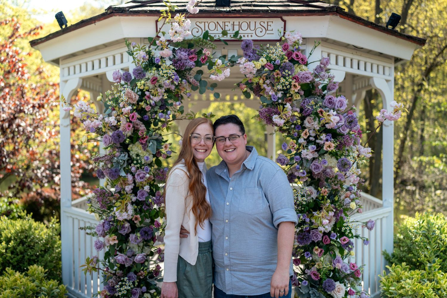 Couple smiling together under floral-covered gazebo arch at Stone House garden venue in spring.