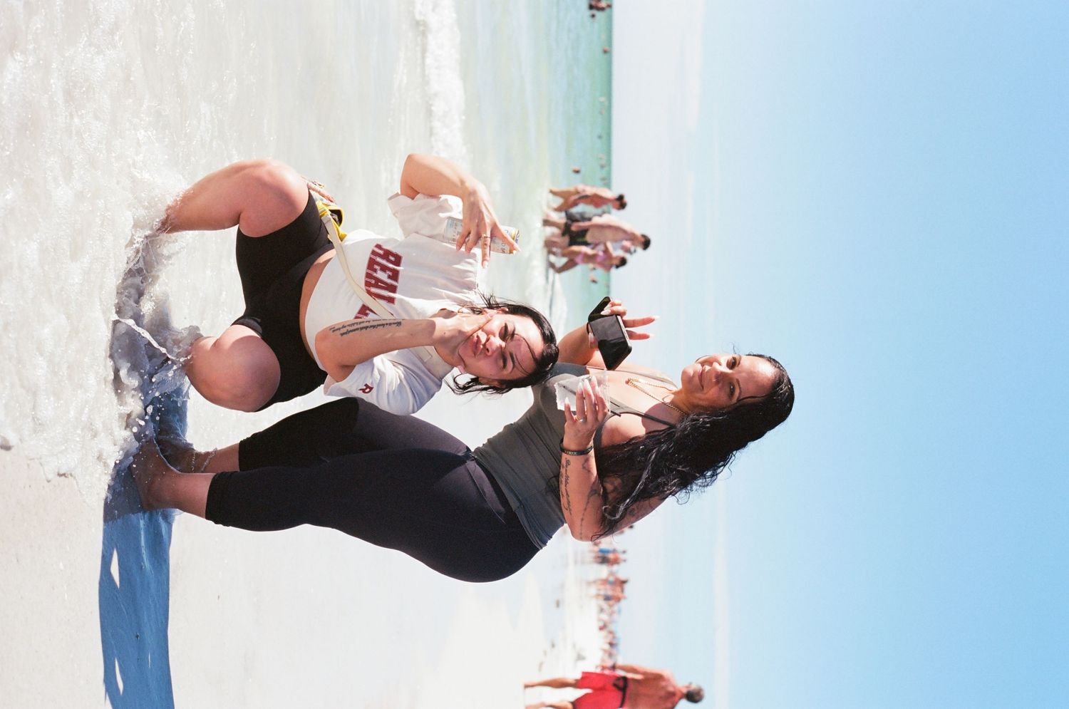 Two young women in swimsuits playing in ocean waves on a sunny beach day.