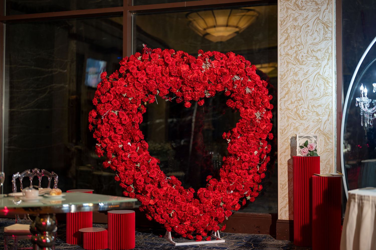 Large heart-shaped floral arrangement made of red roses displayed at a wedding reception venue.