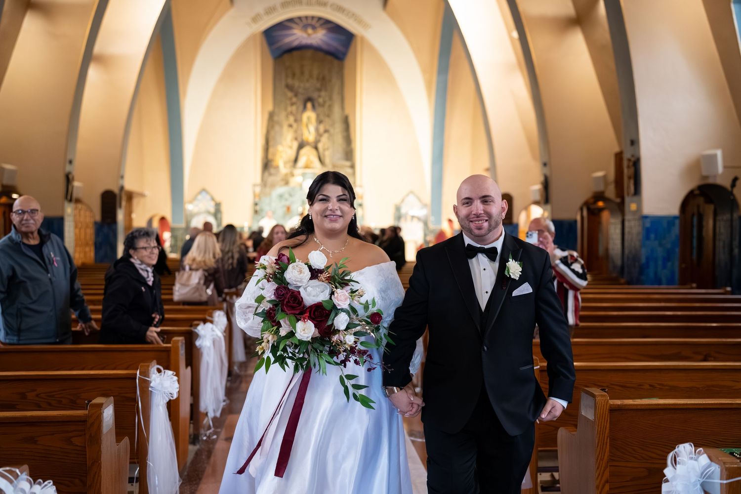 Newlyweds walk hand in hand down church aisle smiling after wedding ceremony.