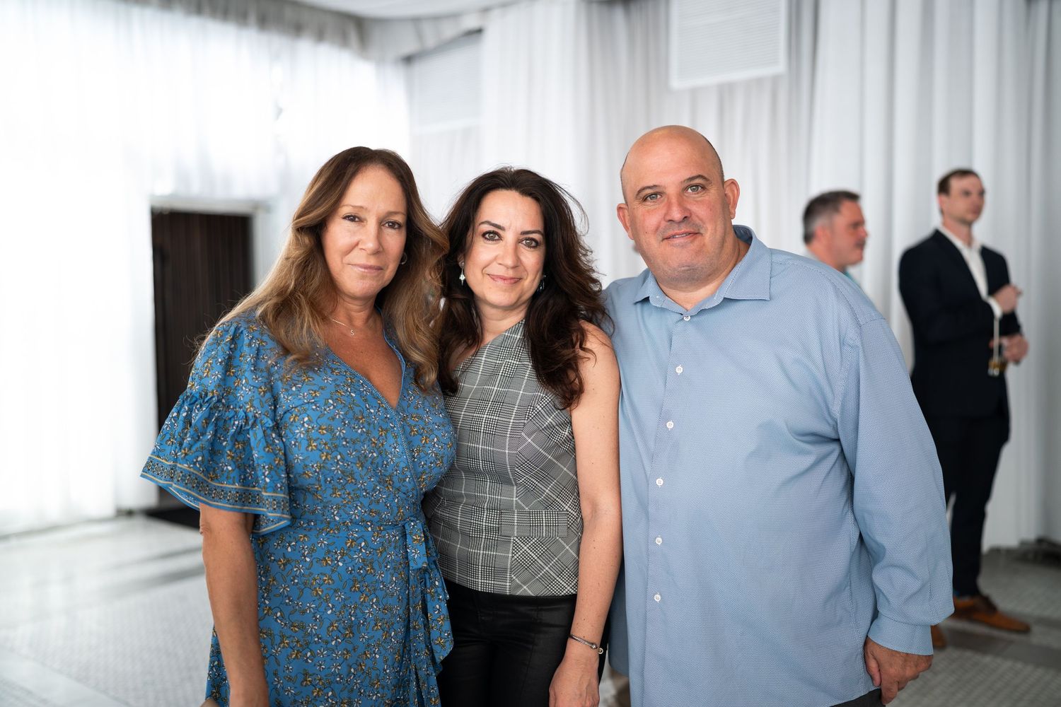 Three people smiling together at an elegant indoor event venue with white decor.