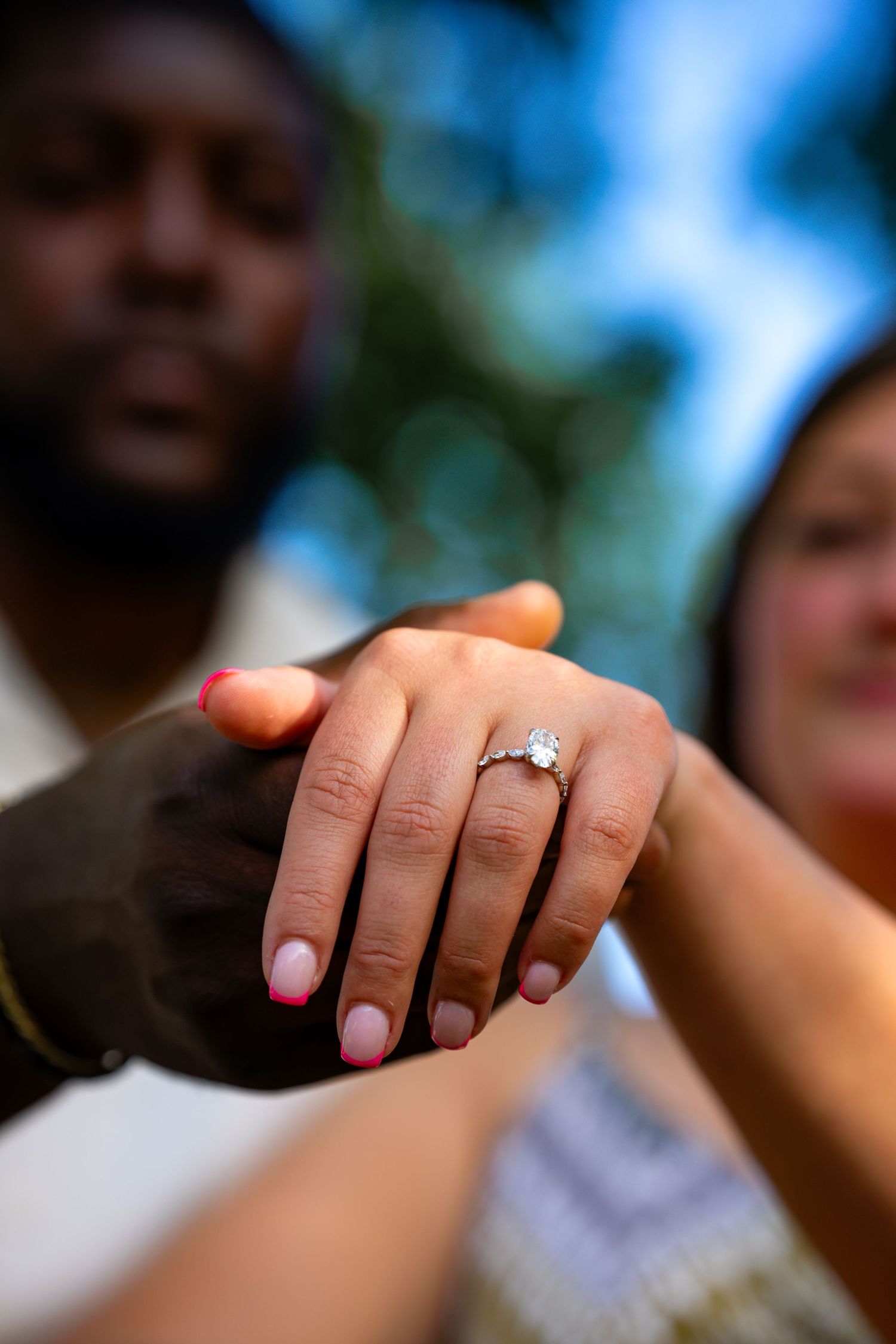Interracial couple displays sparkling oval diamond engagement ring in outdoor setting.