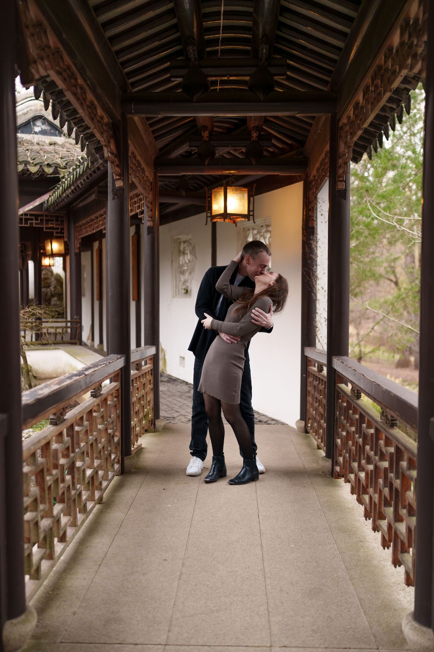 Couple sharing a romantic kiss in an ornate traditional Chinese wooden corridor with lantern lighting.