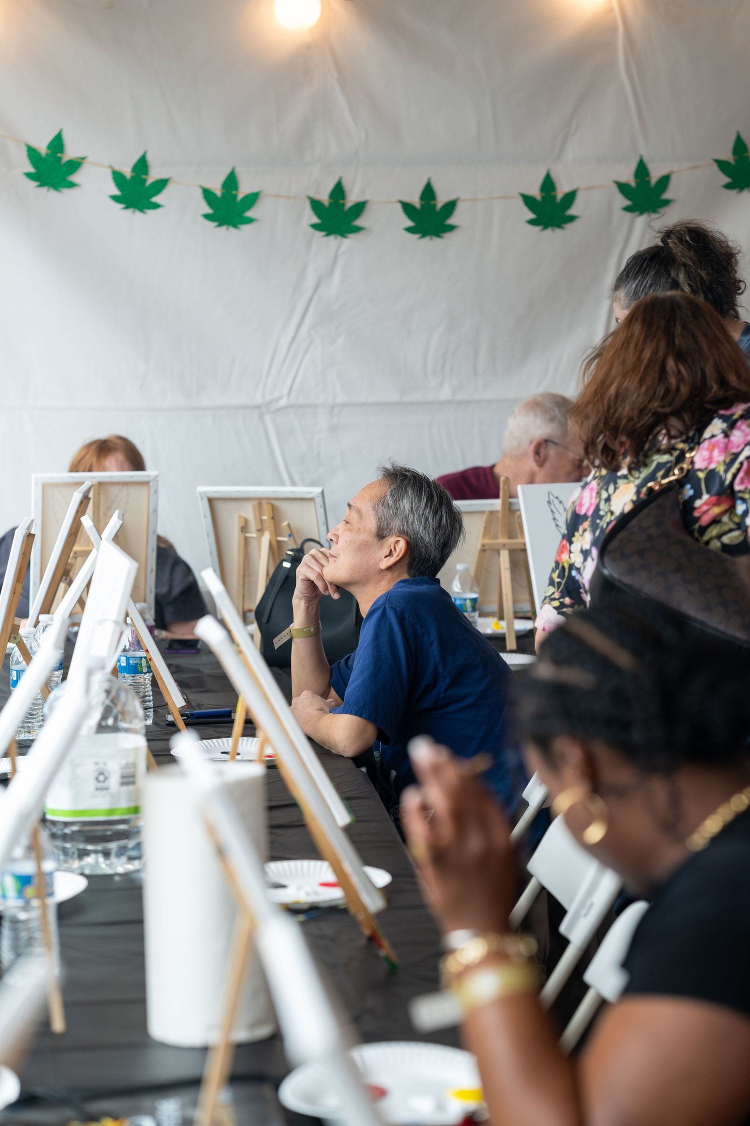 Participants at an art painting class under a tent decorated with cannabis leaf bunting.
