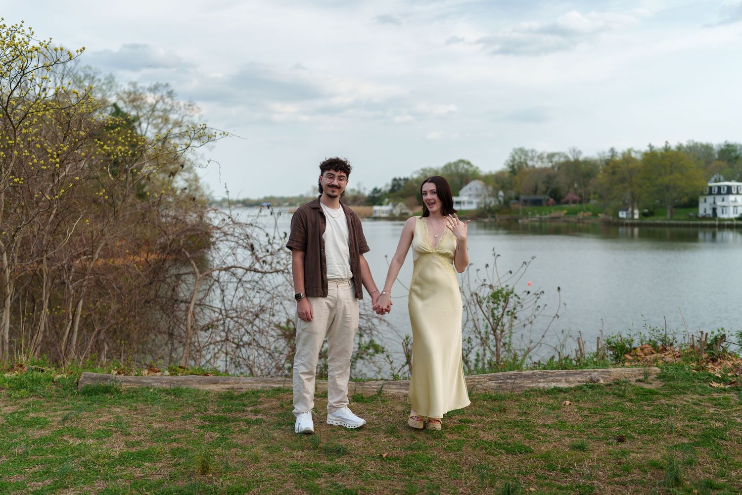 Happy engaged couple holding hands and smiling by a peaceful lake in spring.