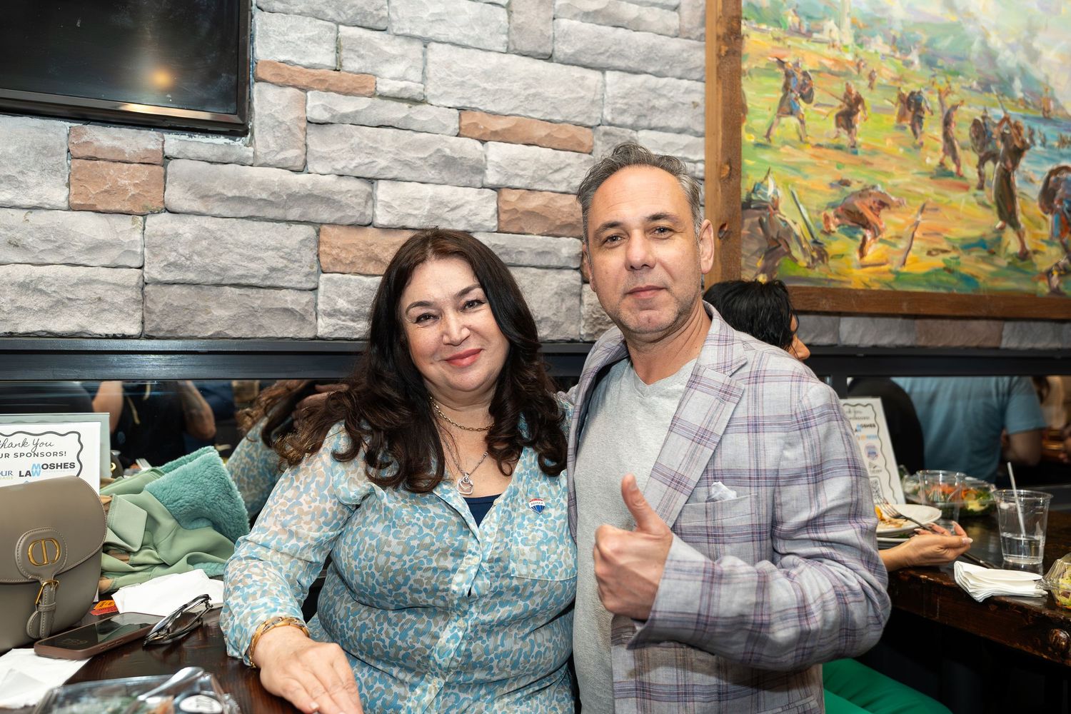 Couple smiling together at a rustic restaurant booth with a painting on the stone wall behind them.