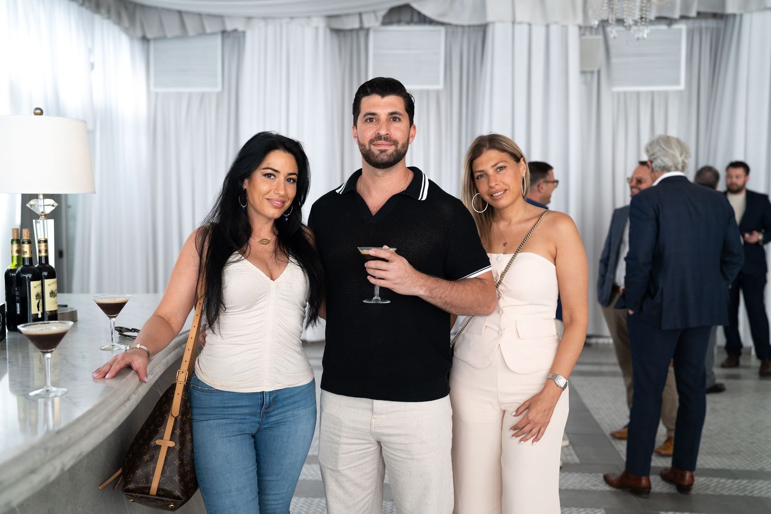 Two women and man holding wine glass pose at elegant event.