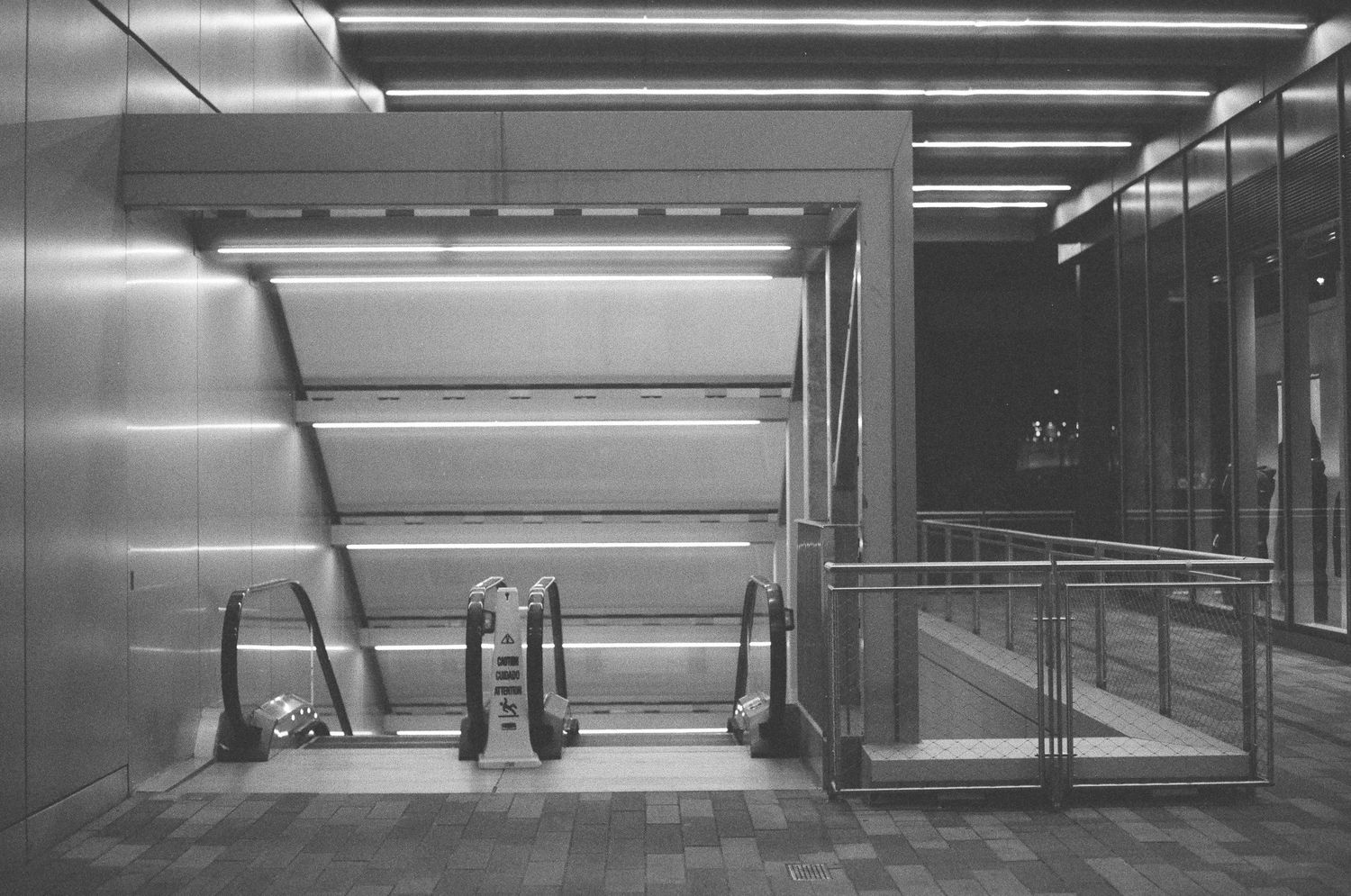 Black and white photo of empty escalators and a ramp in a modern transit station at night.