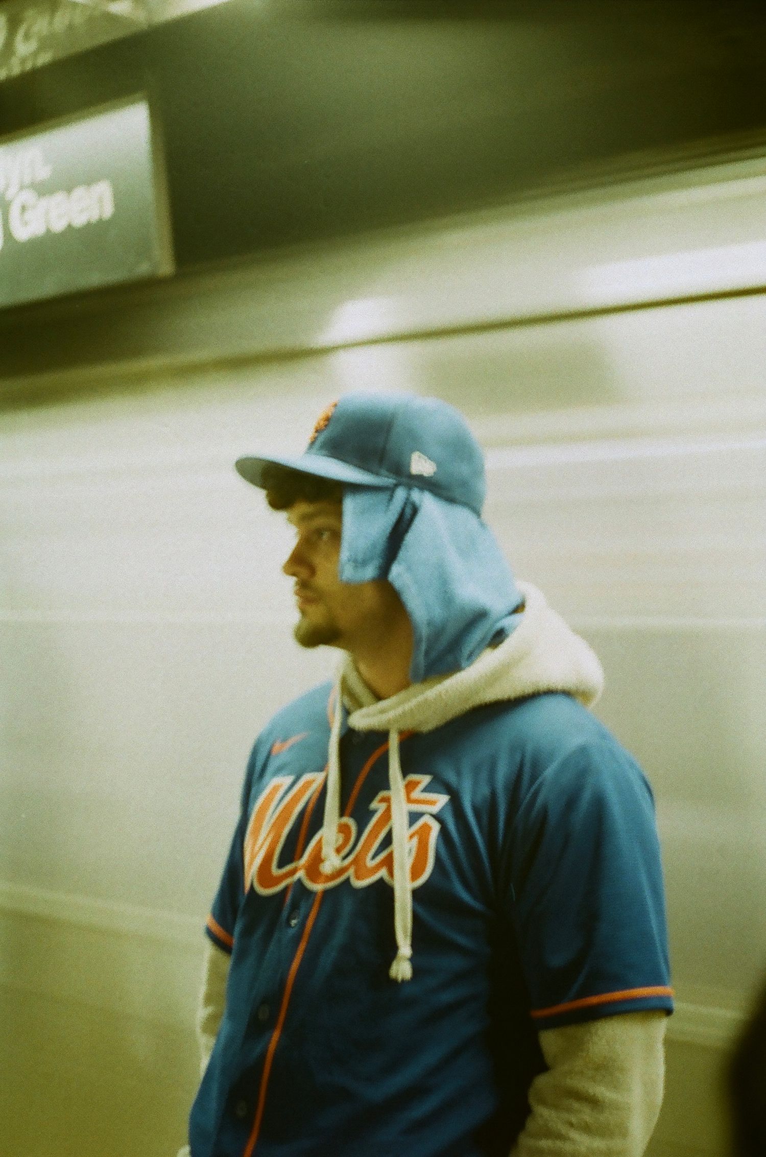Man wearing New York Mets jersey and cap standing in subway station with passing train.