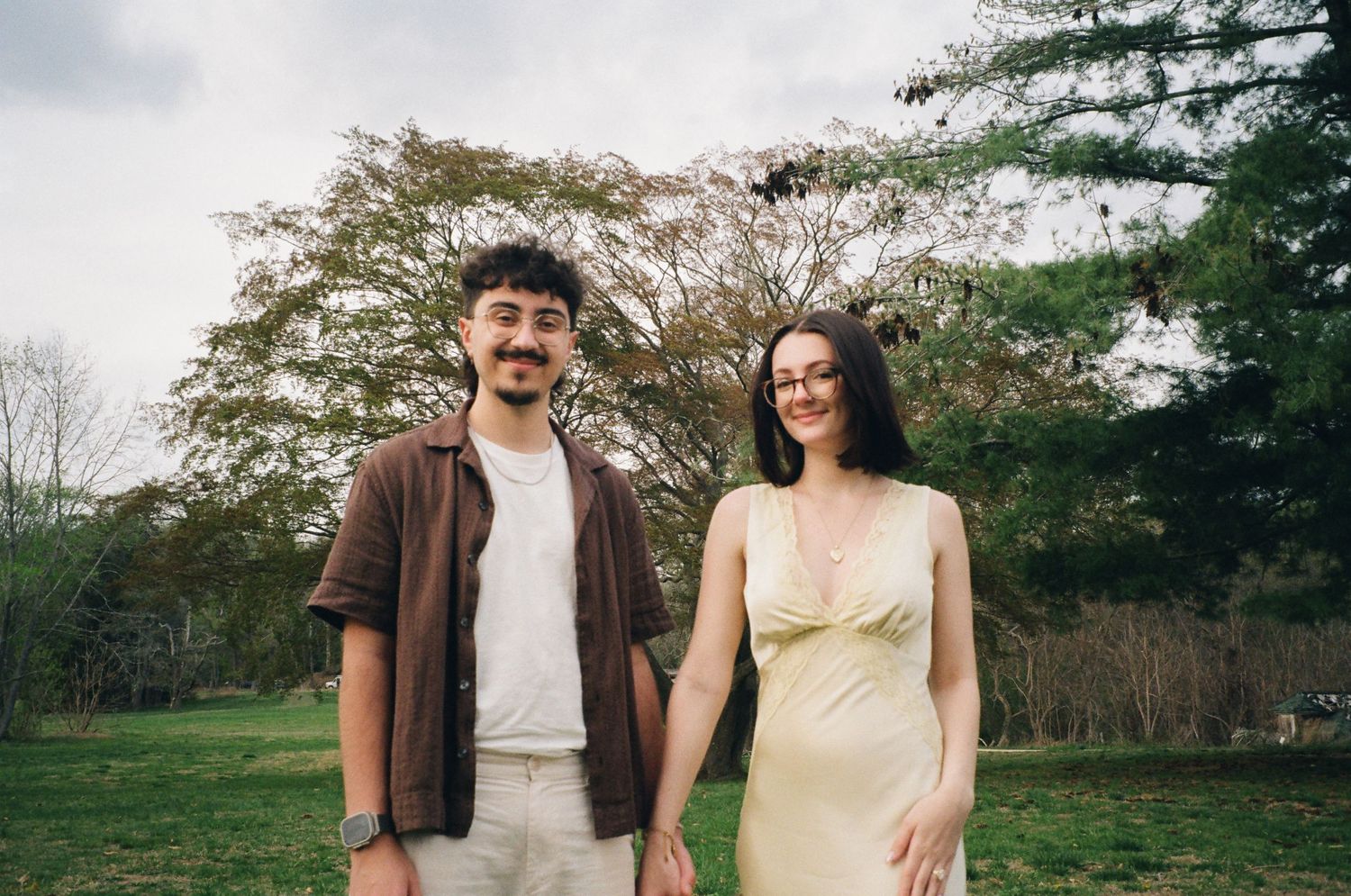 Couple holding hands in a park, man in brown shirt and woman in yellow dress, smiling together.