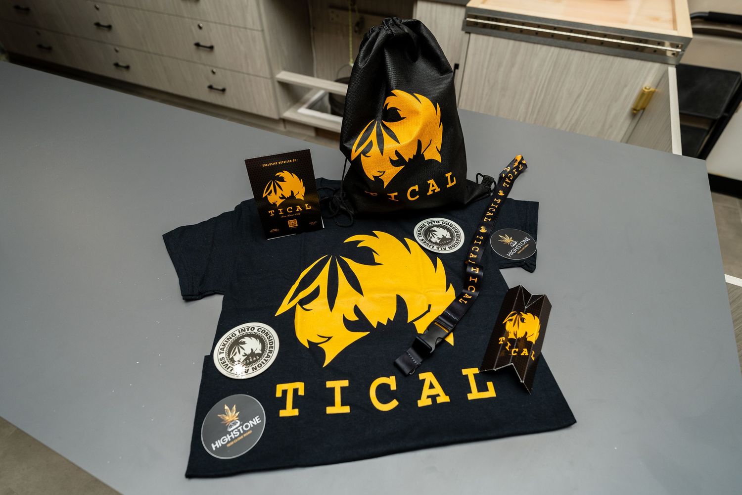 Flat lay of TICAL branded cannabis merchandise including shirt, bag, and accessories.