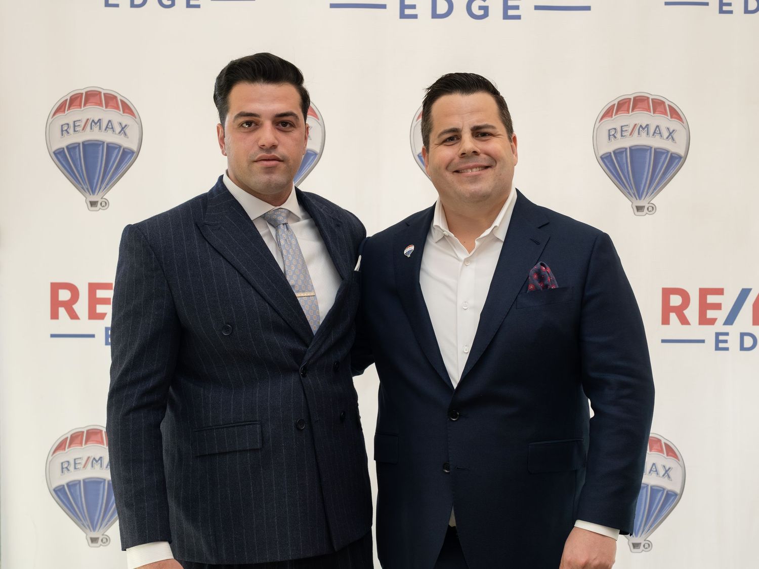Two men in suits pose at RE/MAX Edge real estate office event.