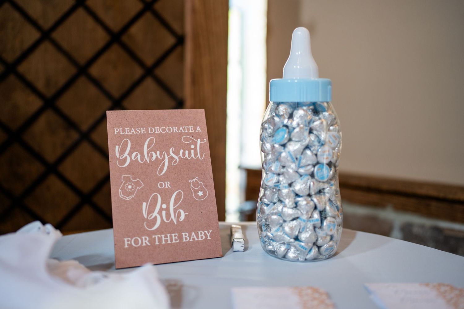 Baby shower table display with large blue bottle filled with Hershey kisses and decorative sign.