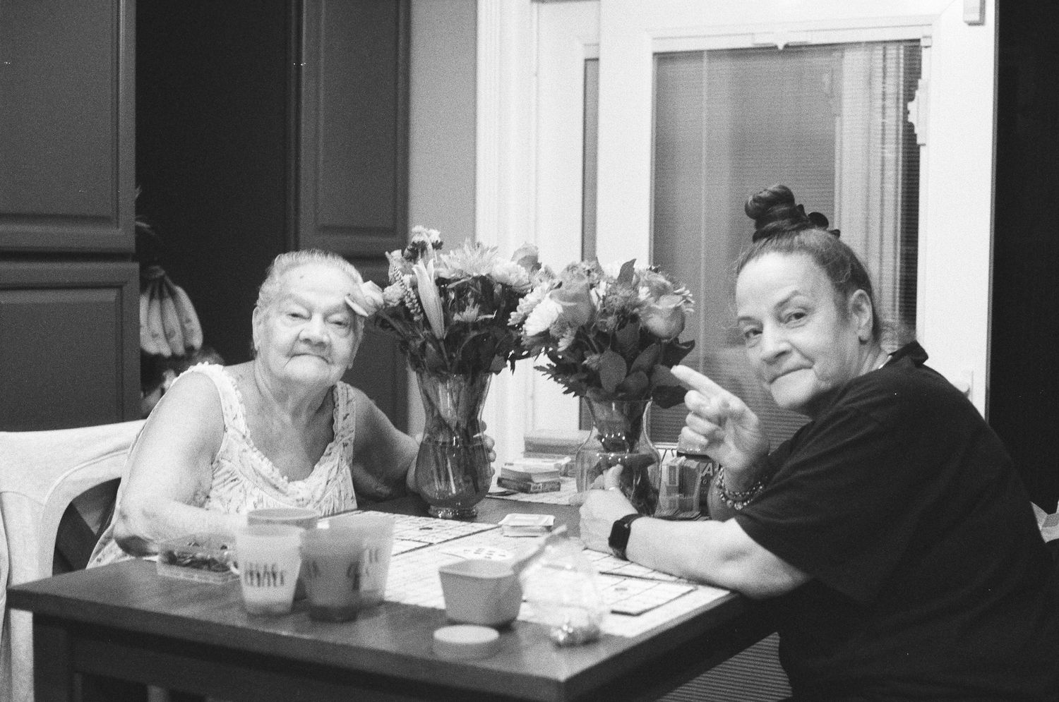 Black and white photo of two people smiling at a dining table with flower arrangement centerpiece.