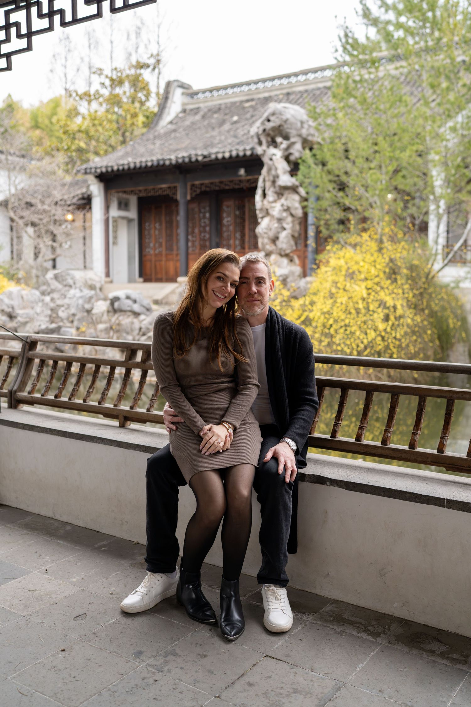 Couple sitting close together on a bench in a beautiful Chinese garden with rock formations.