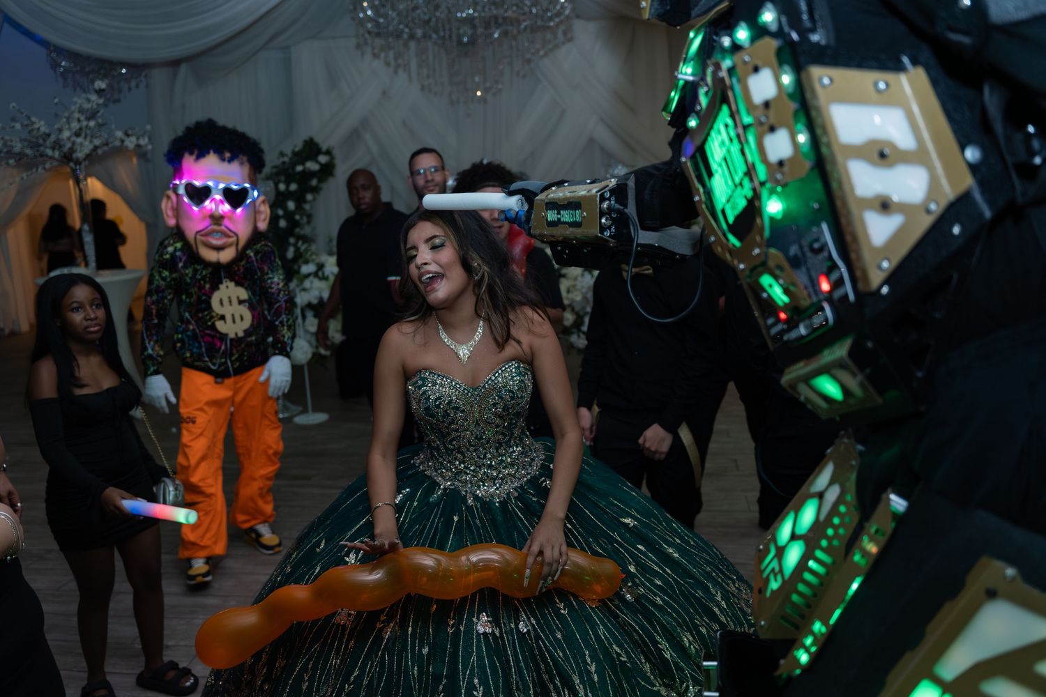 Teen in green ball gown laughs while dancing with masked performers at Sweet 16 party.