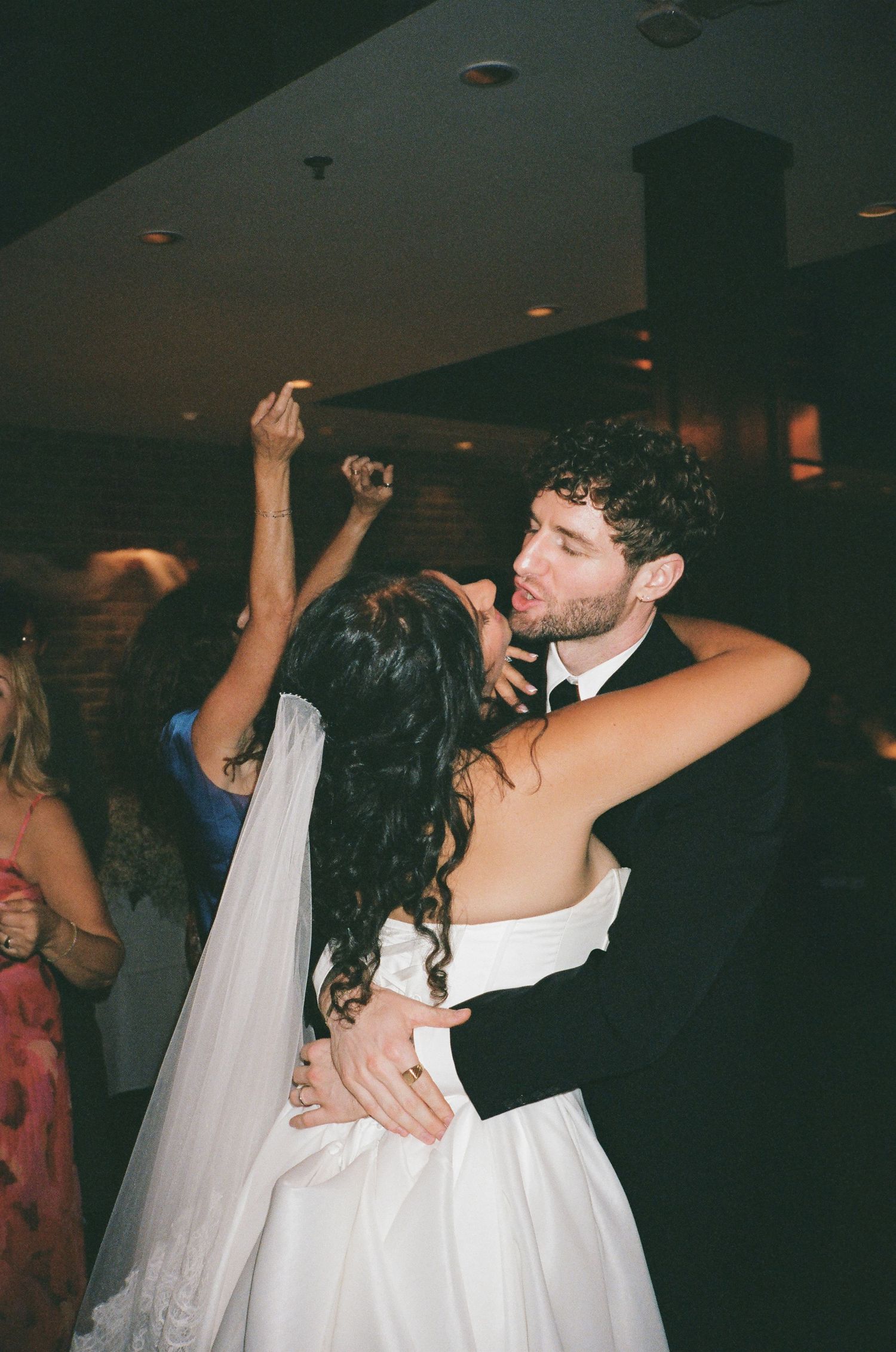 Bride and groom sharing romantic dance embrace at lively indoor wedding reception.