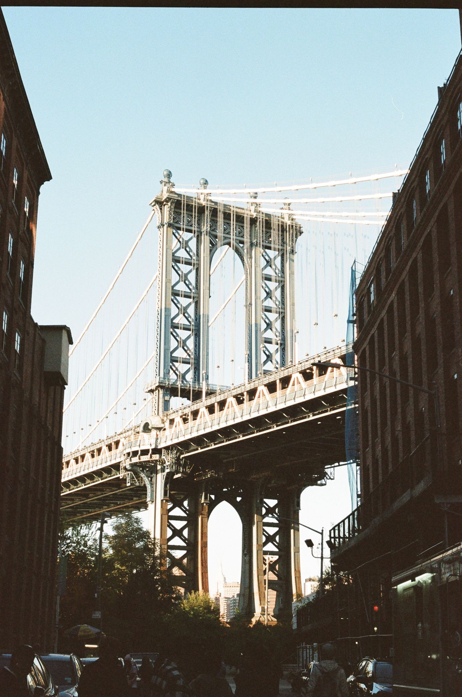 Manhattan Bridge framed between brick buildings in DUMBO Brooklyn on a clear day.