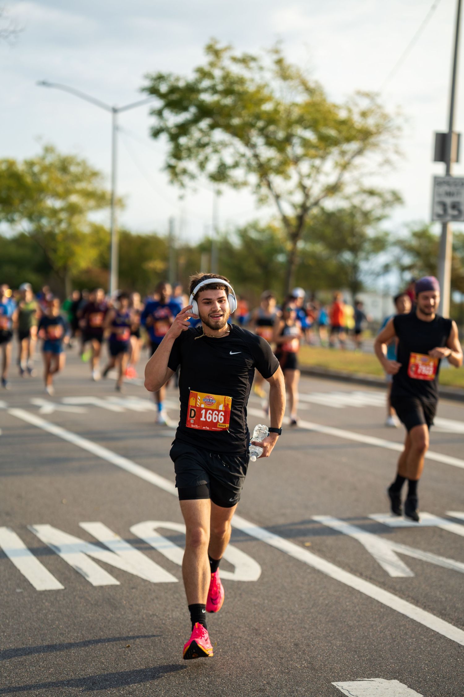 Male marathon runner number 1666 smiling while racing on a sunny urban road.