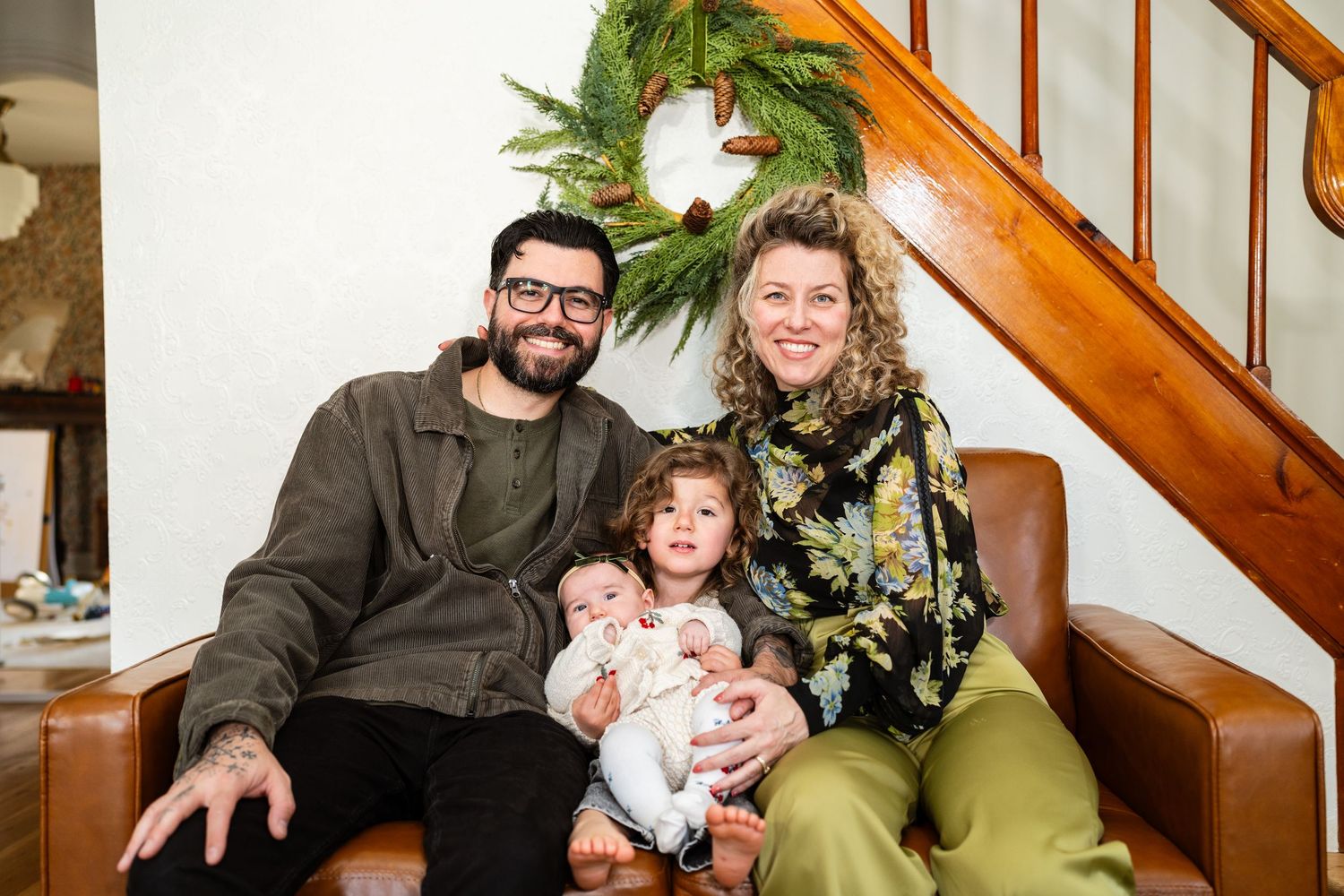 Happy family of four posing on leather sofa with Christmas wreath on staircase.