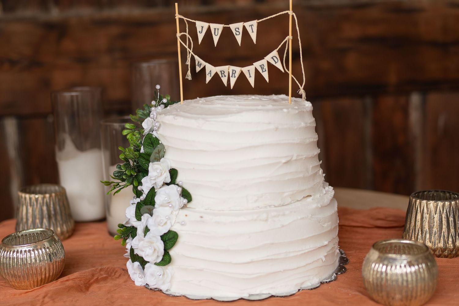 Elegant two-tier white wedding cake with floral accents and rustic banner topper.