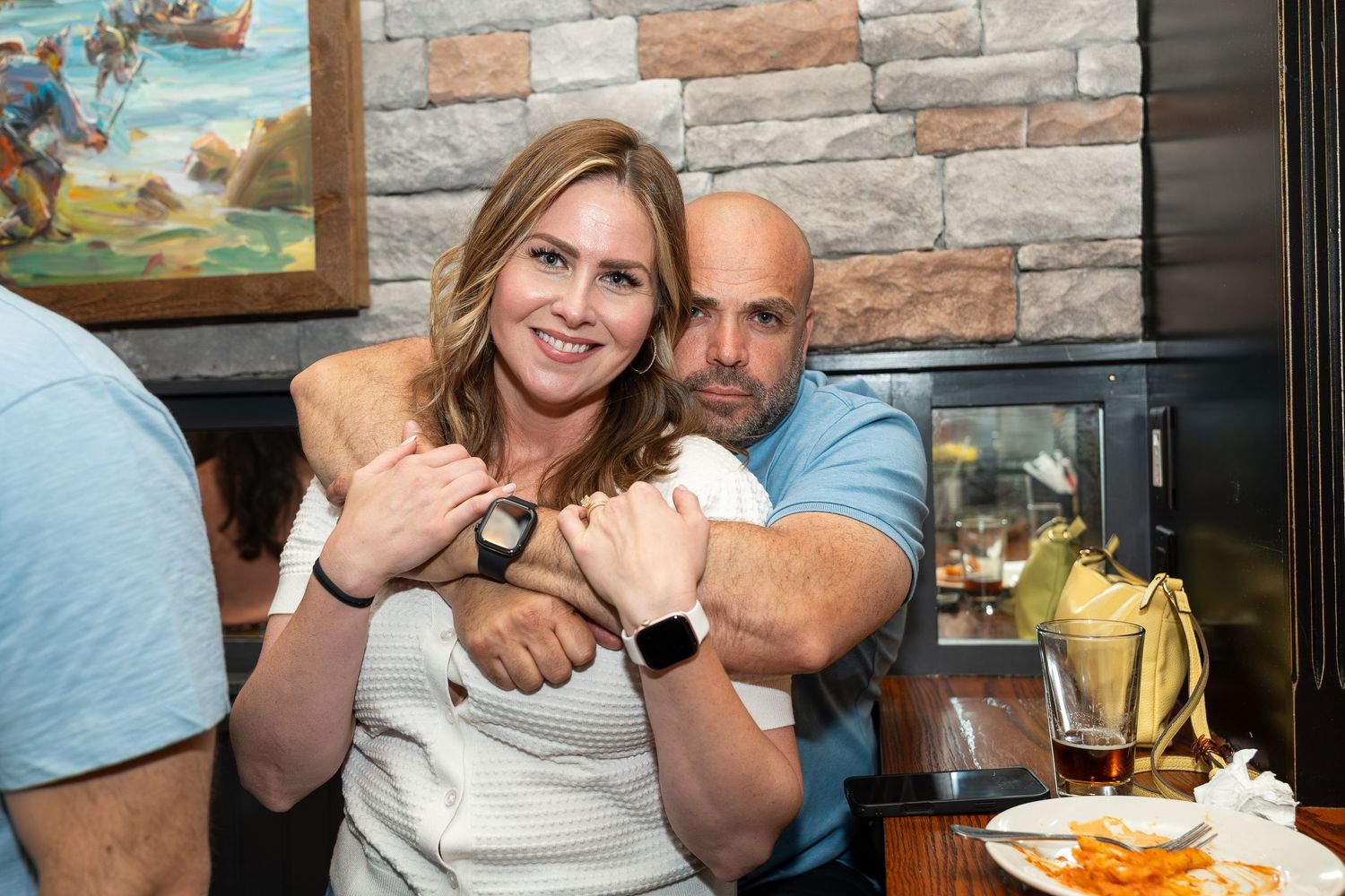 Smiling couple showing off matching smartwatches while sitting together at a restaurant.