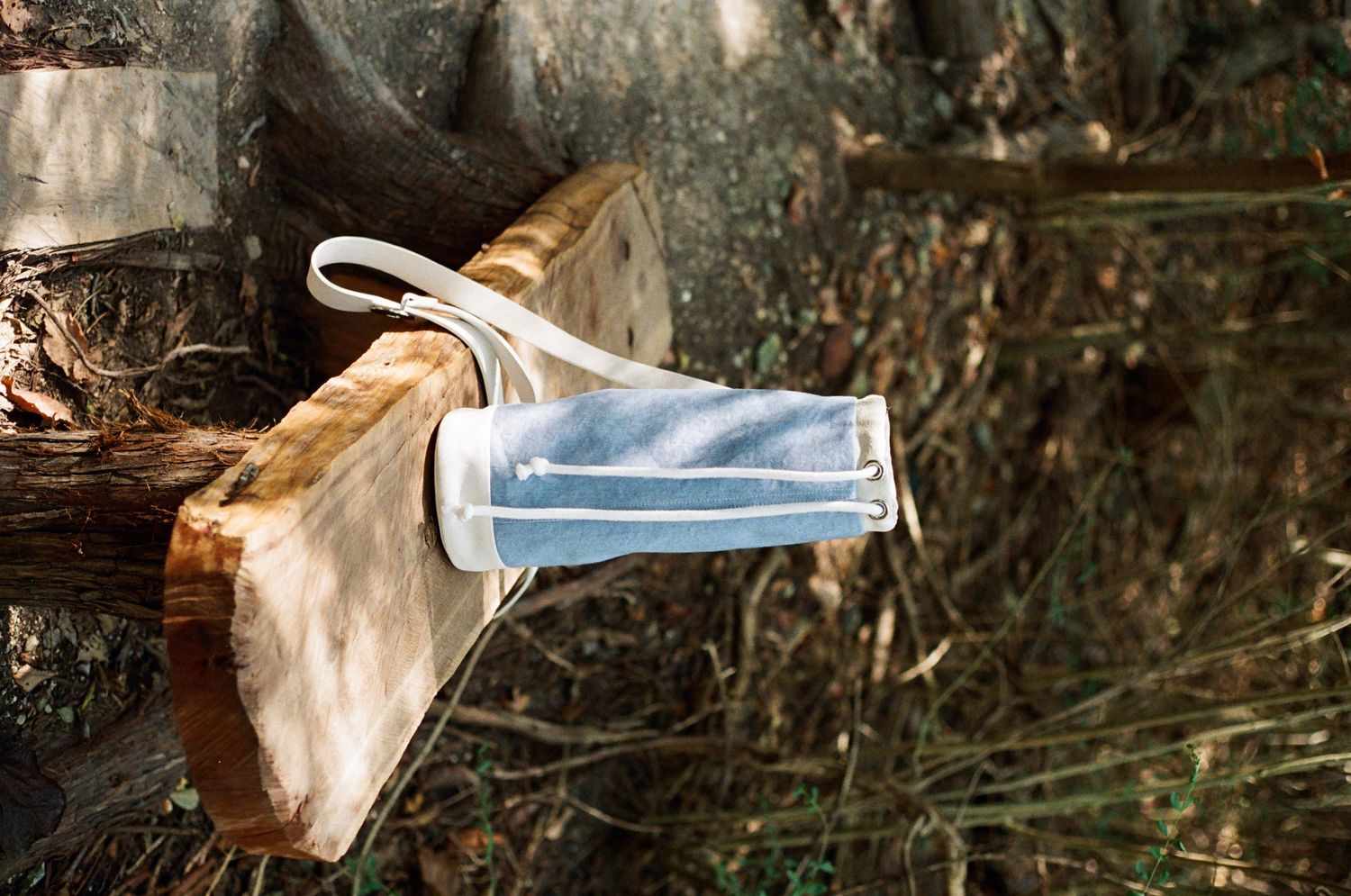 A blue disposable face mask hanging on a wooden log in a natural outdoor setting.