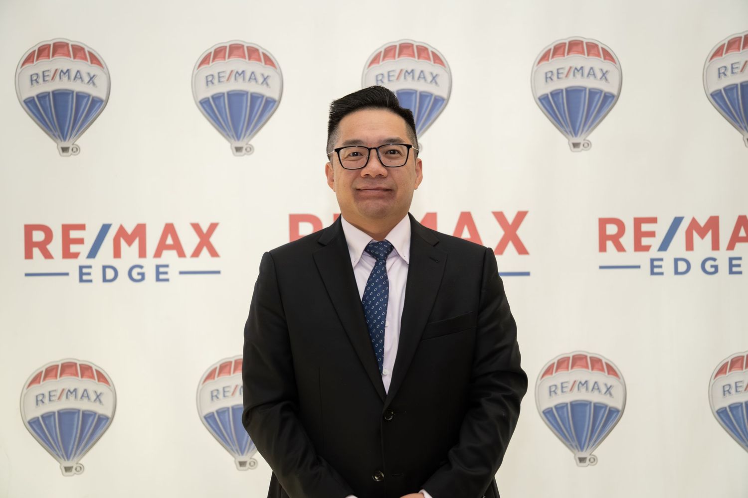 Real estate professional in a suit posing in front of RE/MAX Edge branded backdrop.