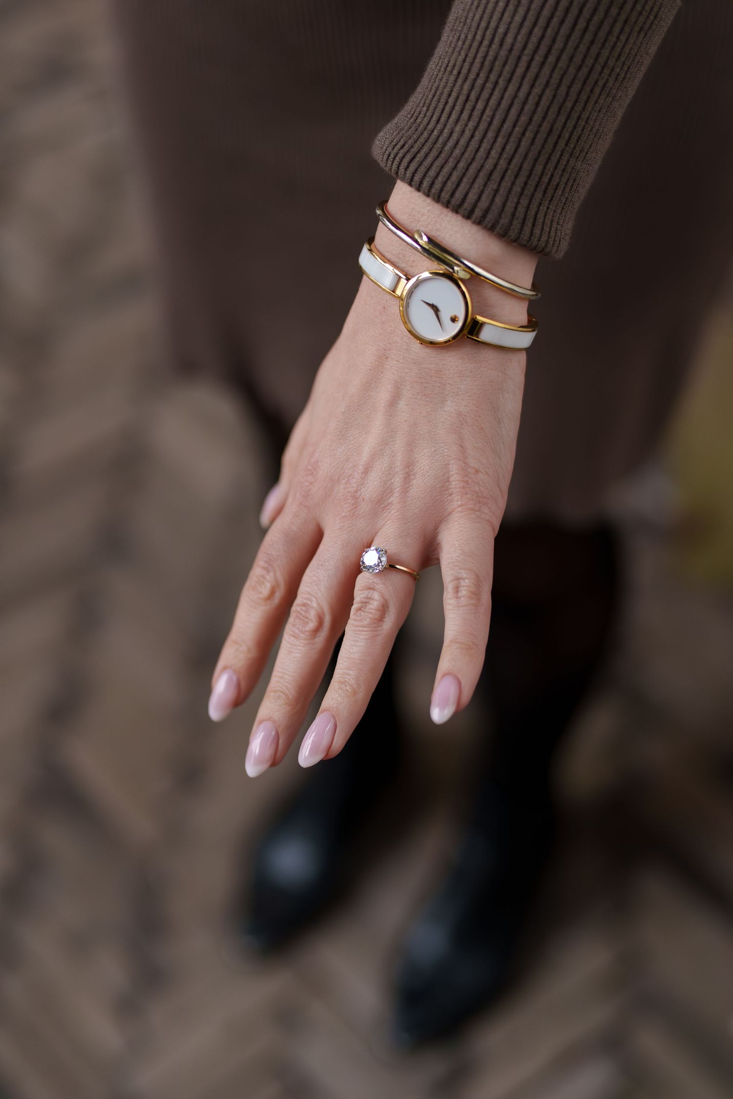 Close-up of woman's hand displaying an engagement ring alongside a gold and white wrist watch.