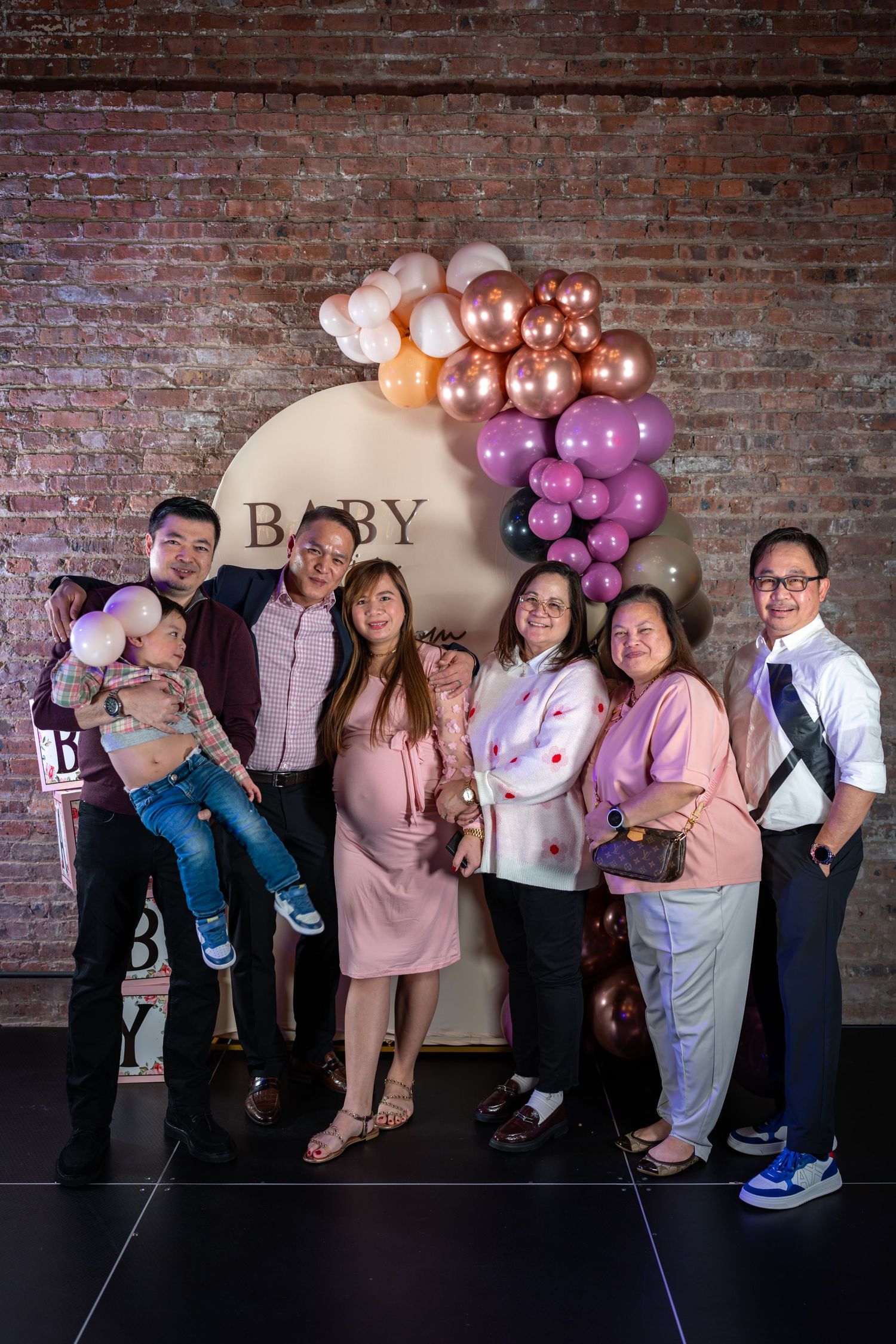 Group of family and friends posing together at a baby shower in front of a balloon arch backdrop.