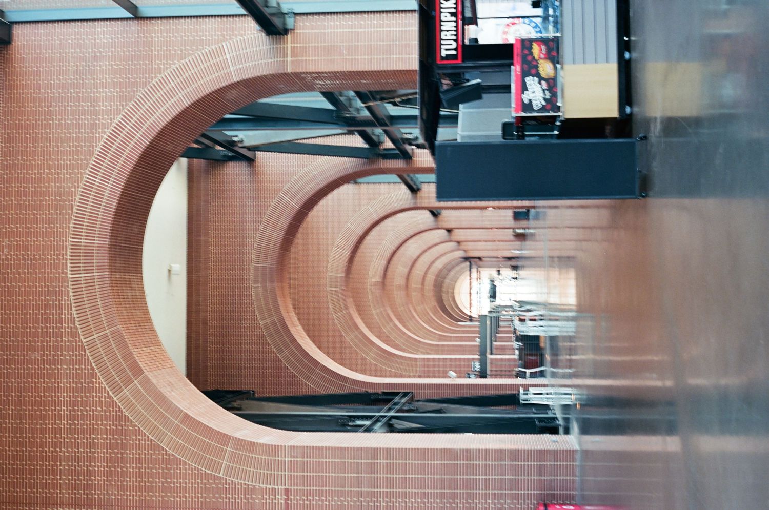 Vertical perspective of repeating brick arches in a shopping mall corridor with retail signs.