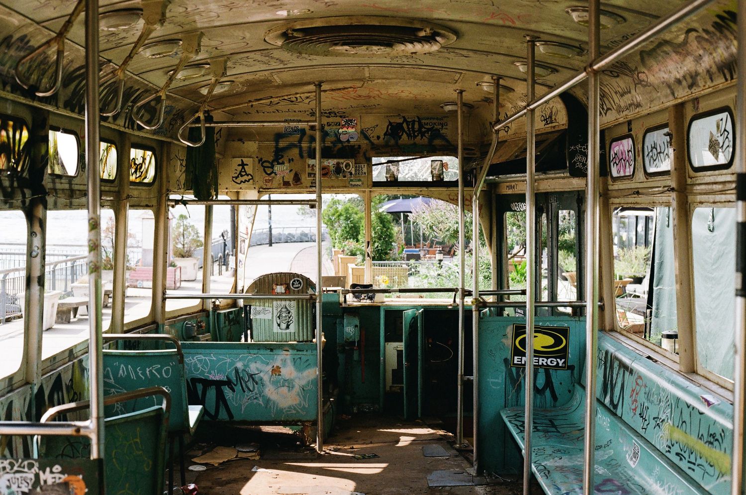 Interior of an abandoned graffiti-covered vintage trolley car with green seats and peeling paint.