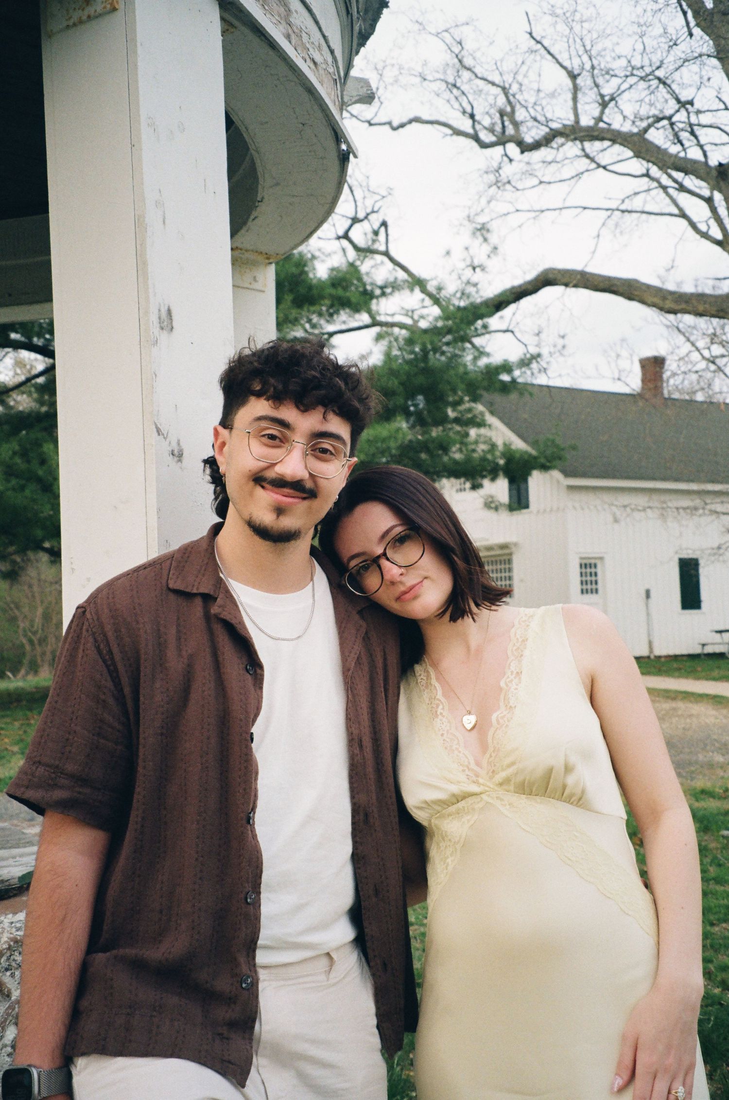 Couple smiling closely together outdoors near a white structure with a historic building in background.