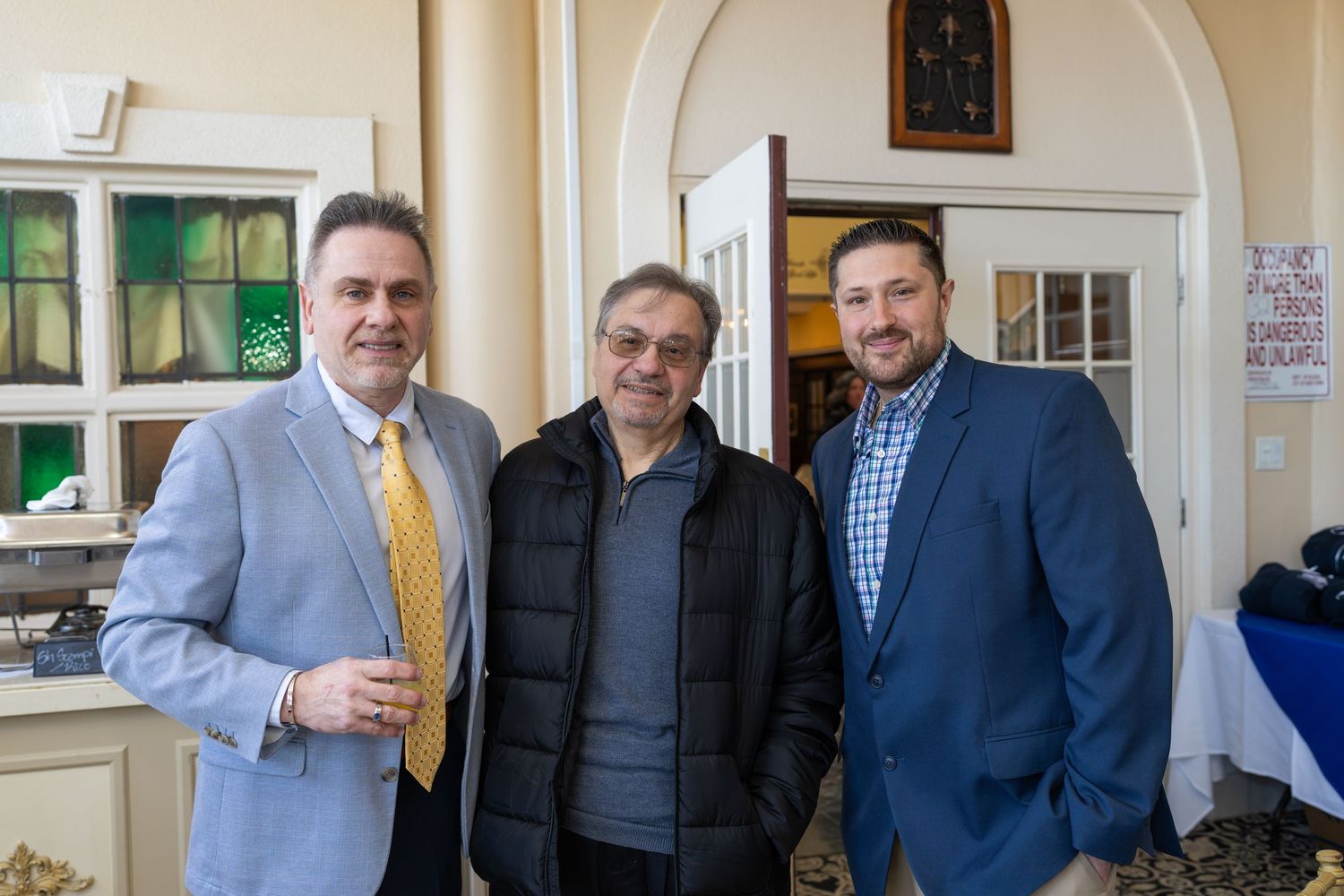 Three men in blazers smiling together at a RE/MAX Edge real estate networking event.