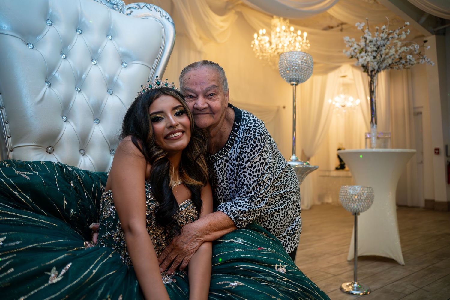 Young woman in green quinceañera gown poses with older man on decorative throne chair.