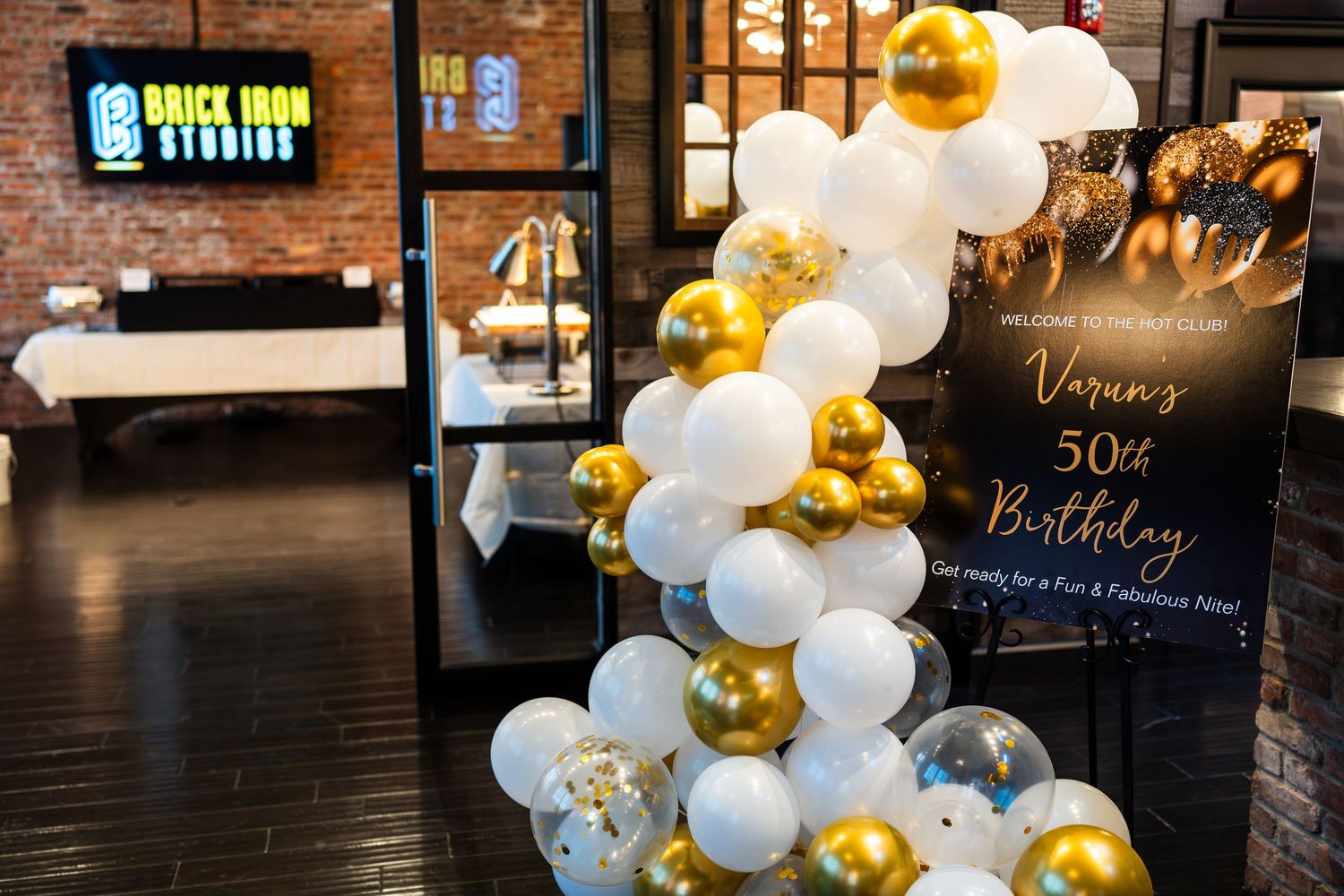 Elegant white and gold balloon arch display next to a 50th birthday celebration sign at Brick Iron Studios.