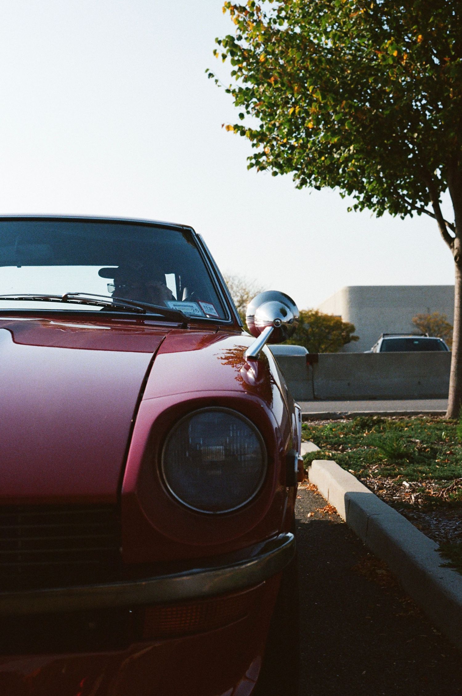 Front view of classic vintage red car parked near curb with trees in background.