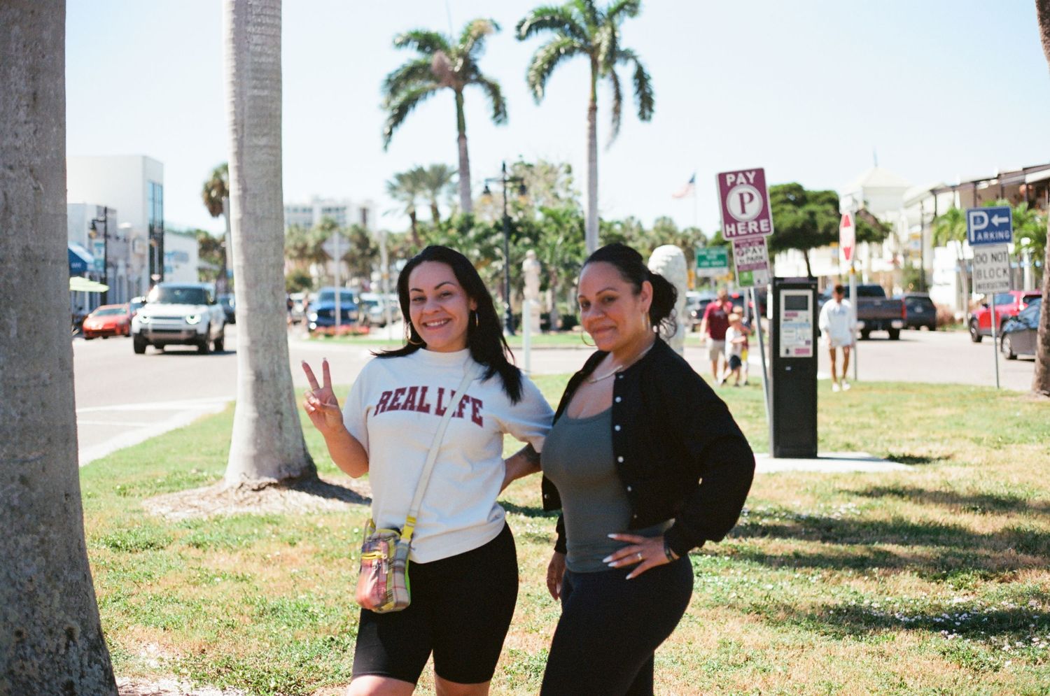 Two young women pose and smile on a sunny palm tree-lined street near Venice Beach, California.