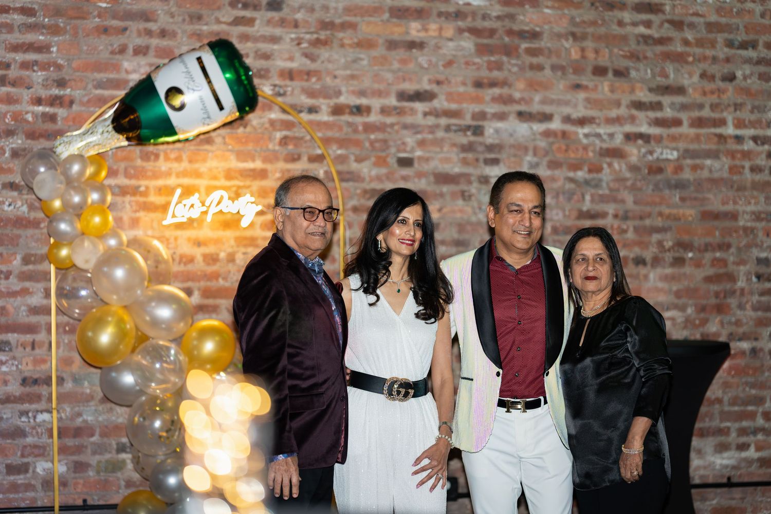 Four guests posing together in front of a champagne bottle balloon display and neon 