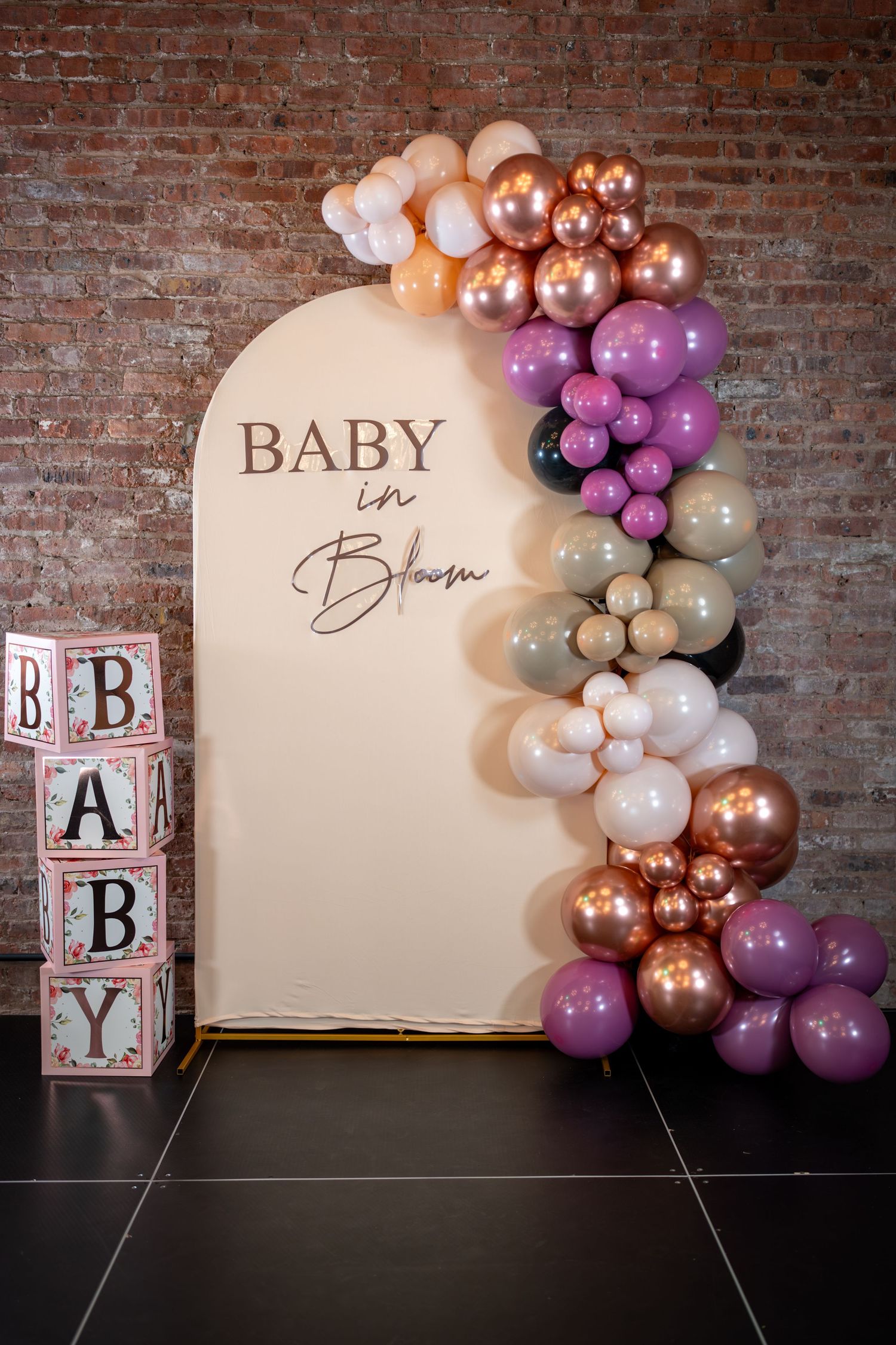 Baby shower backdrop with balloon garland in rose gold, purple, and white, featuring a 