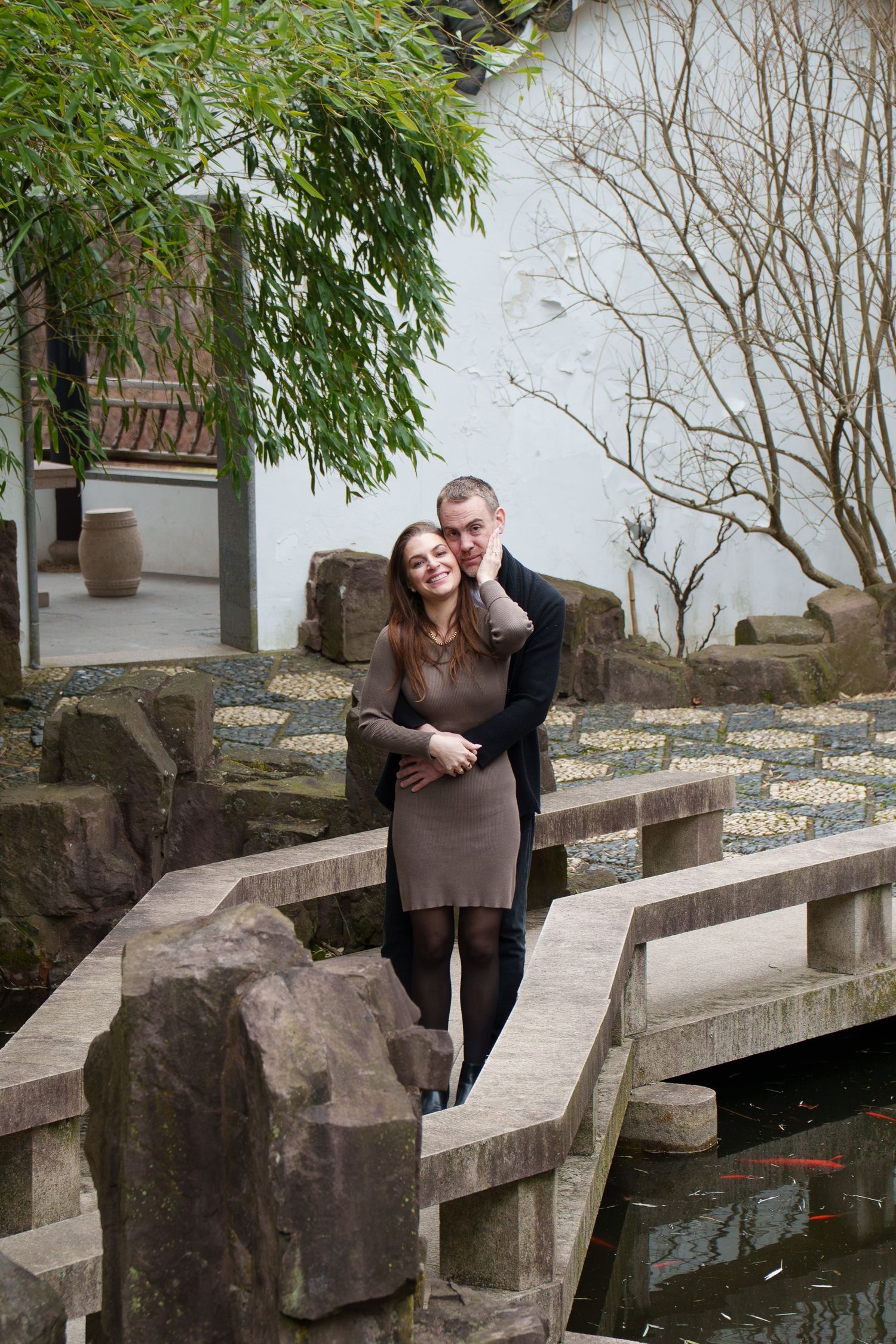Happy couple cuddling on a stone bridge over a koi pond in a Chinese garden.