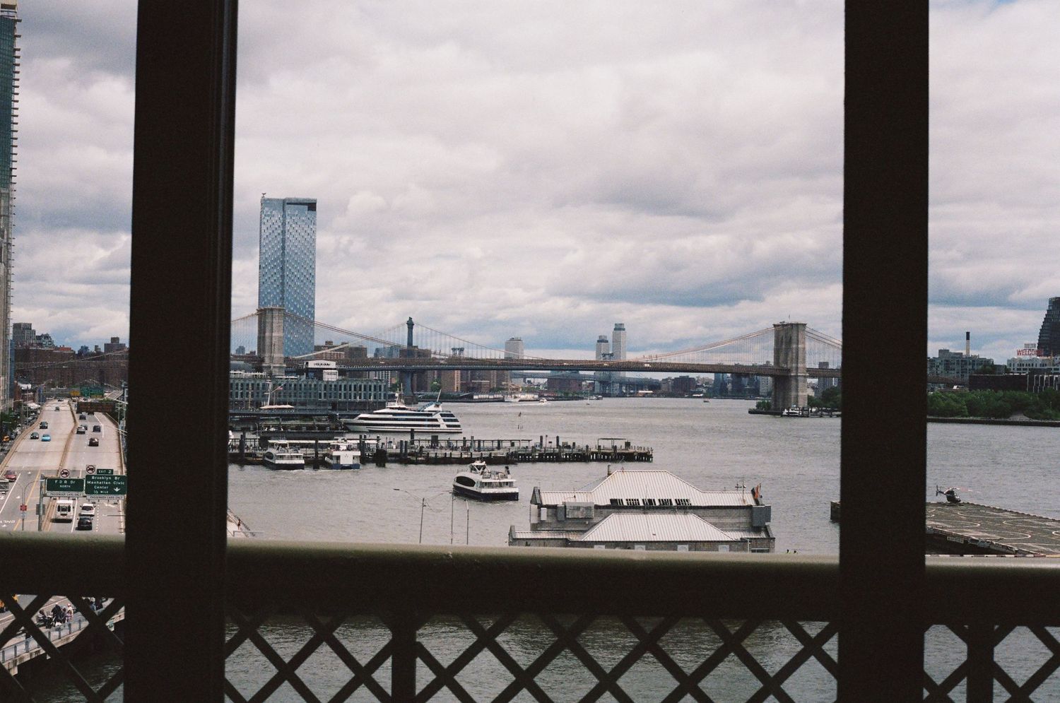 View of New York City waterfront with Brooklyn Bridge and skyscrapers seen through a latticed window.