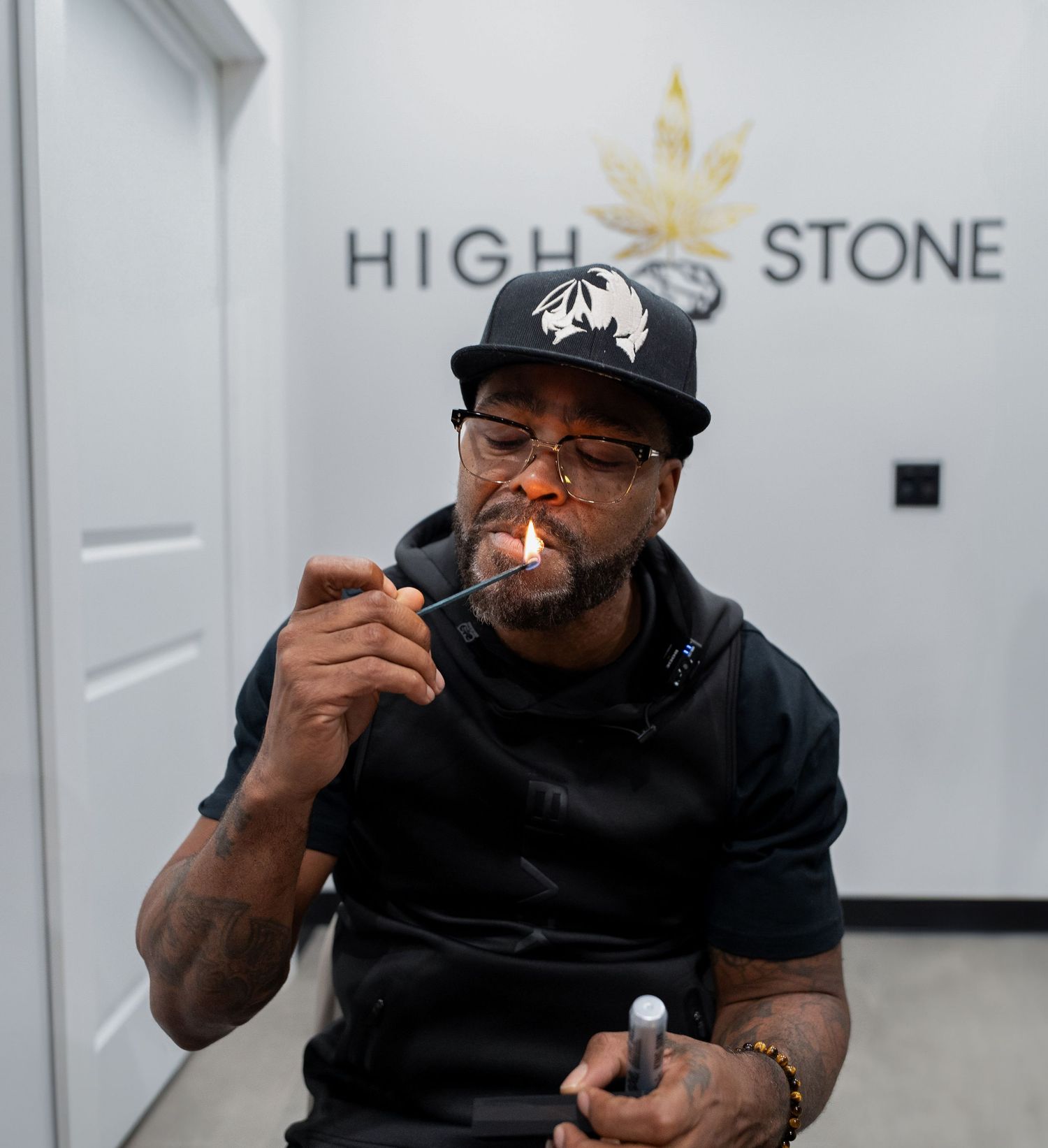 Man lighting a cannabis joint inside a High Stone dispensary storefront.