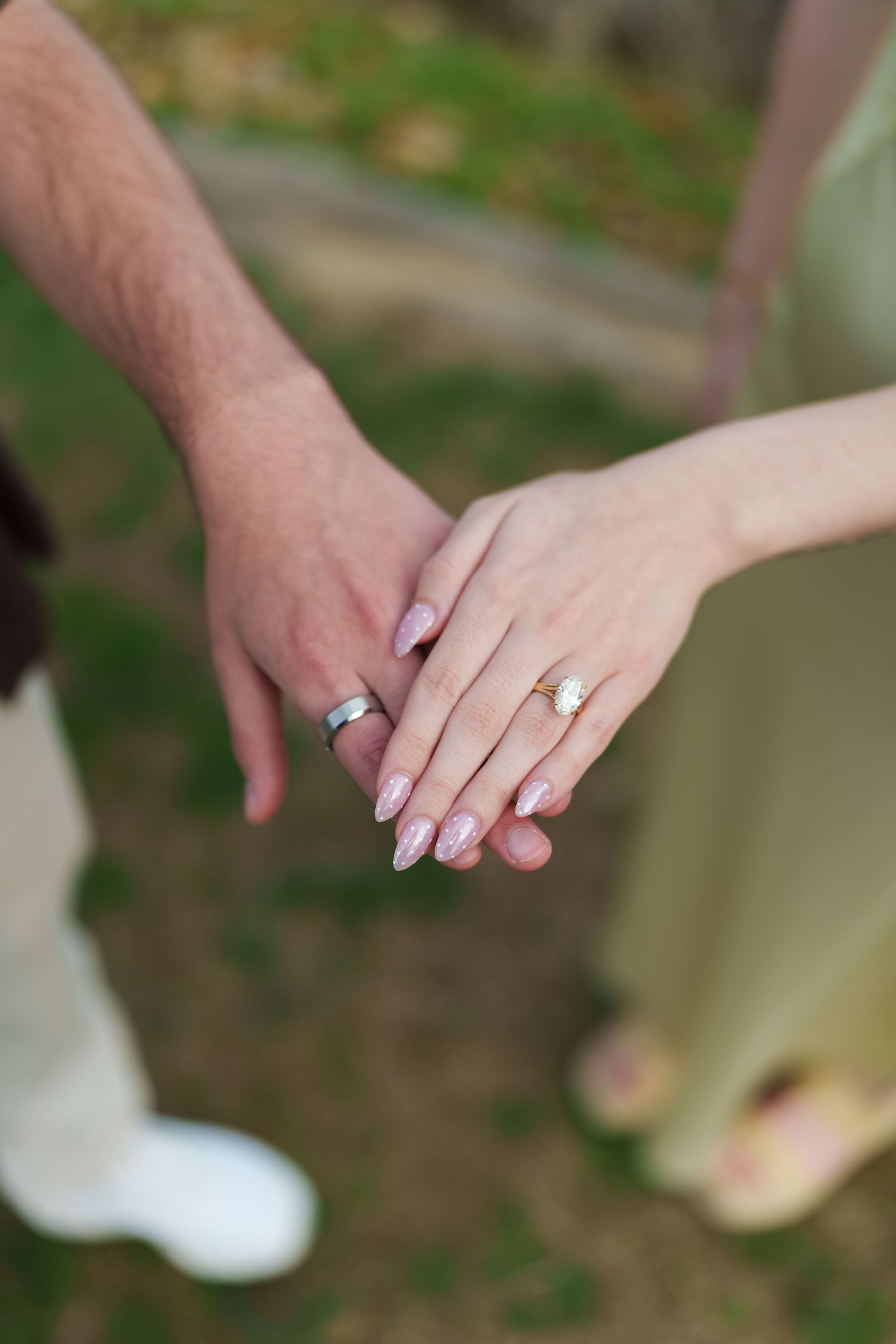 Close-up of couple holding hands showing engagement ring and wedding band outdoors.