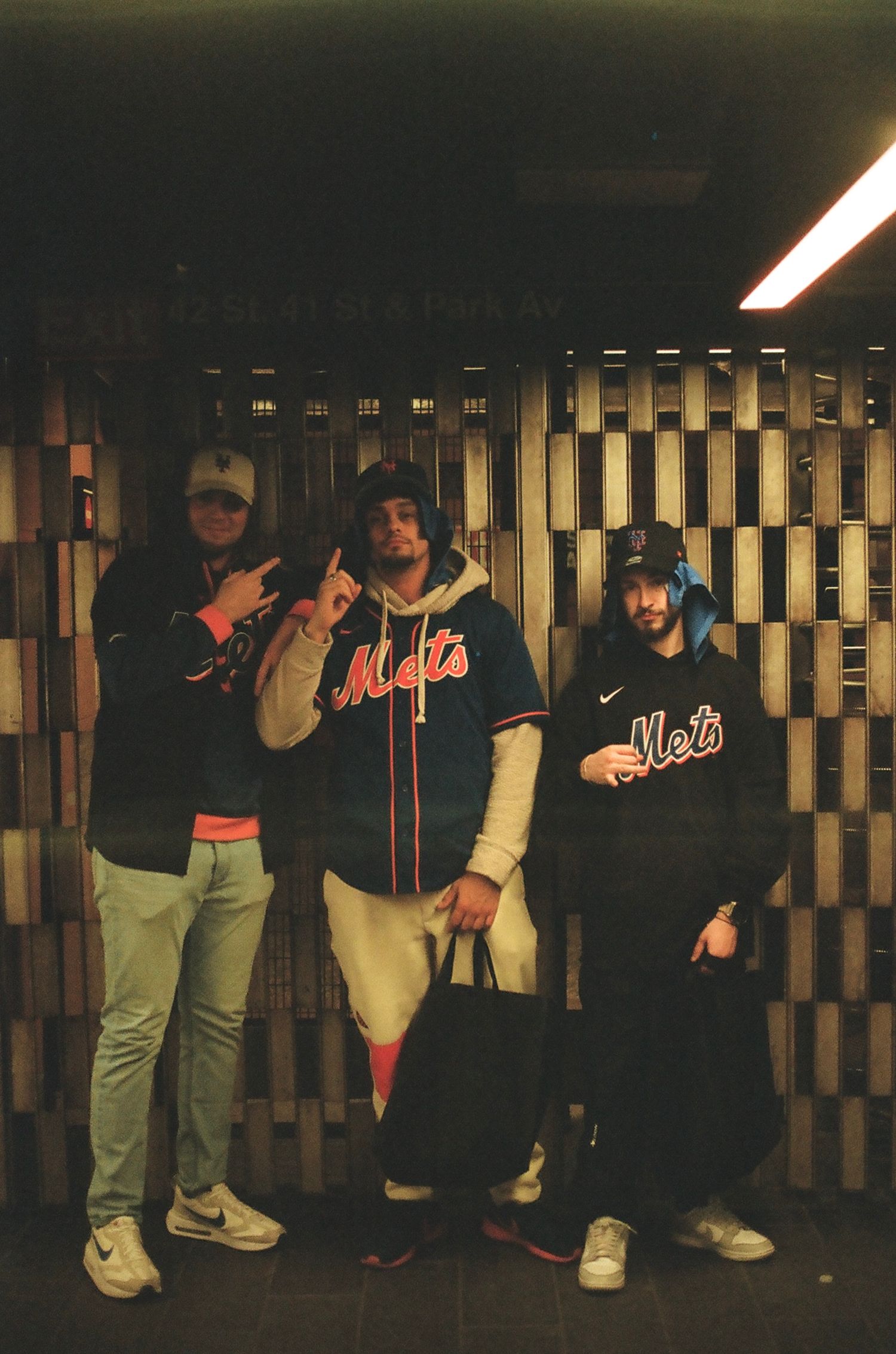 Three New York Mets fans posing in jerseys at a subway station in New York City.