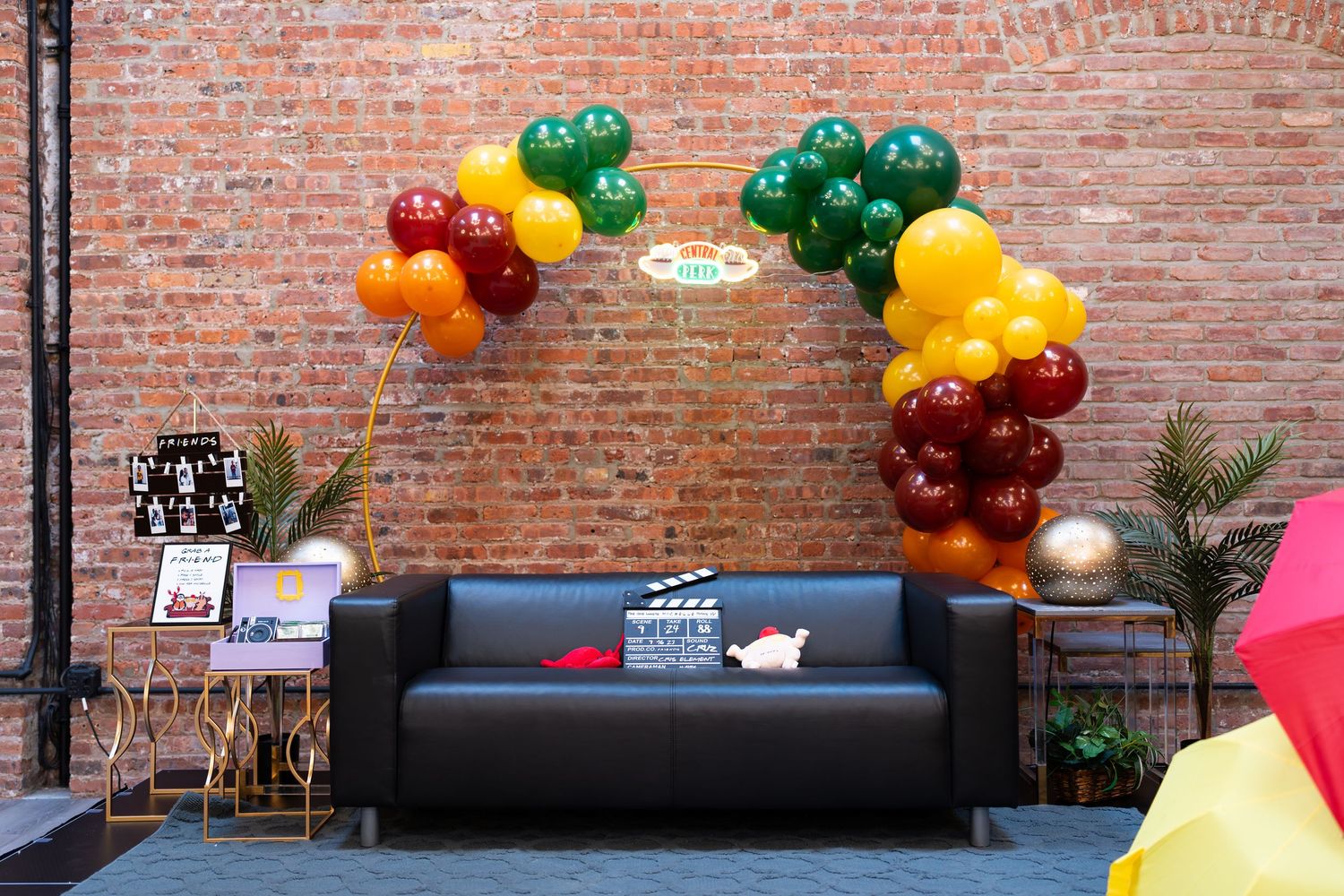 Colorful red, yellow, and green balloon arch over a black sofa with a movie clapperboard theme decor.