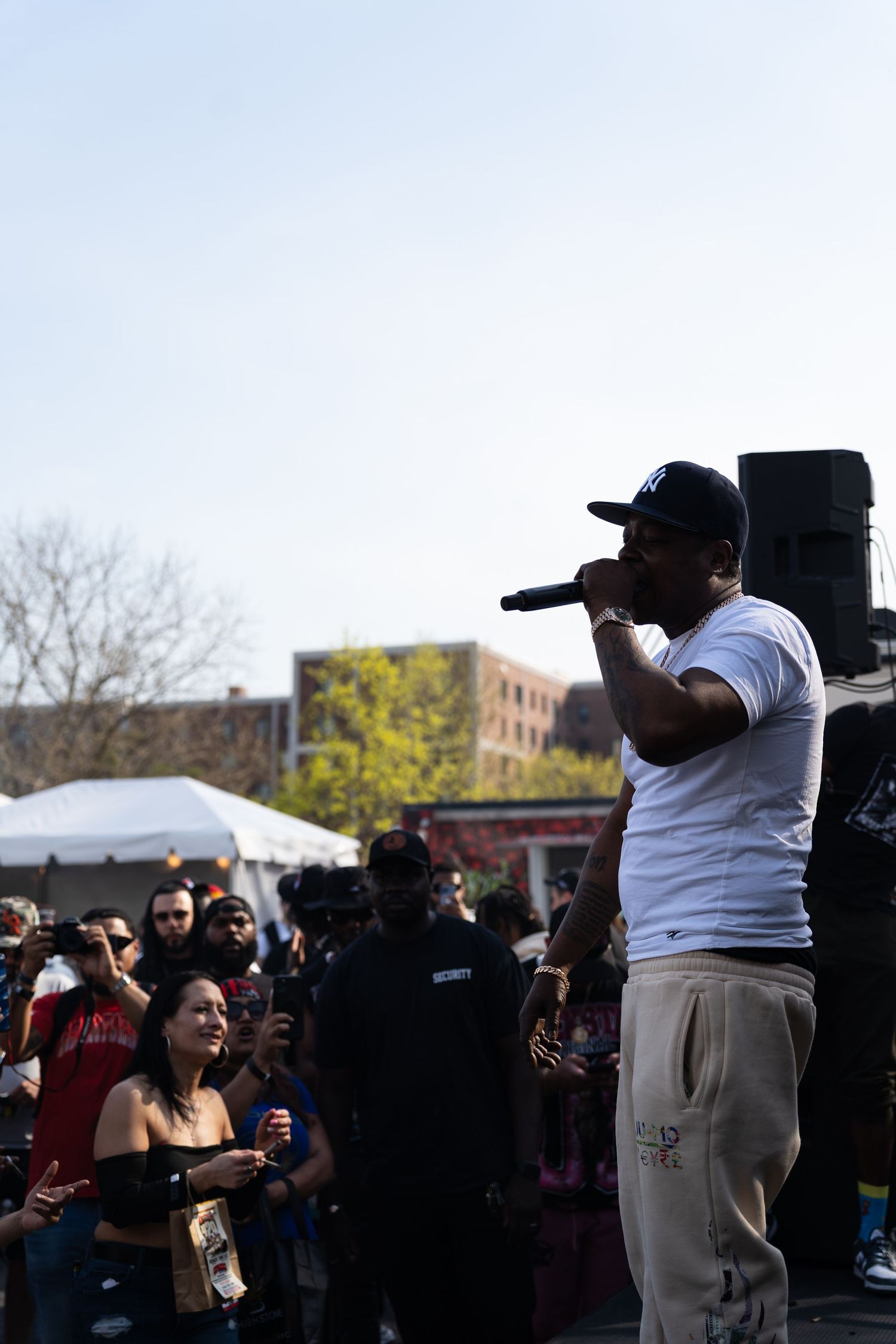 Hip-hop artist performing on outdoor stage with microphone before a large crowd on a sunny day.